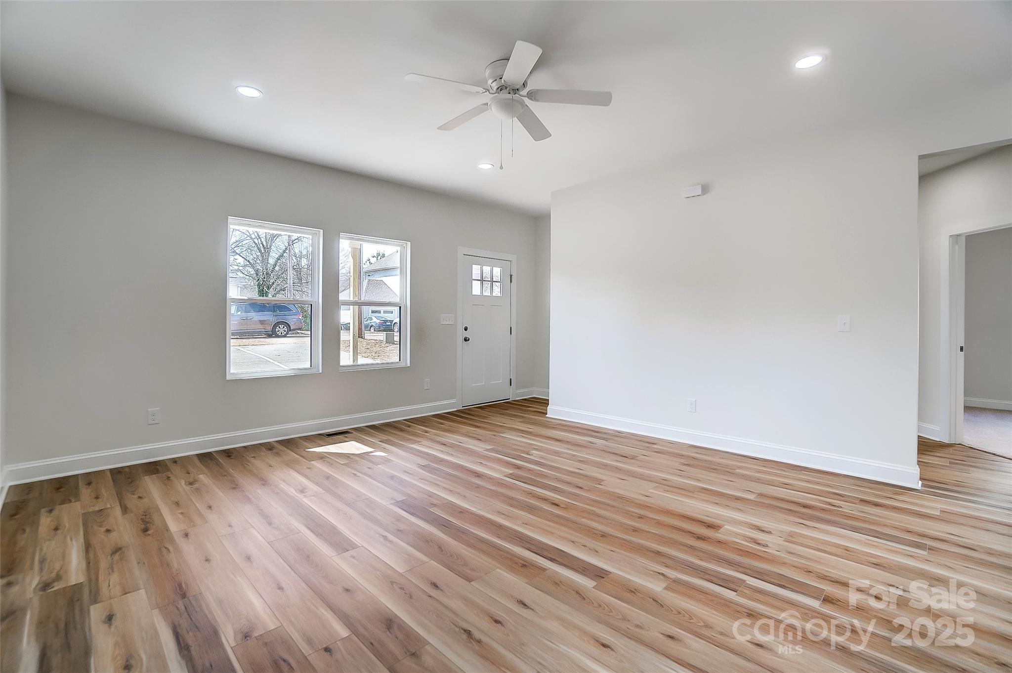 Vacant living room with wood plank flooring, two windows, and a ceiling fan.