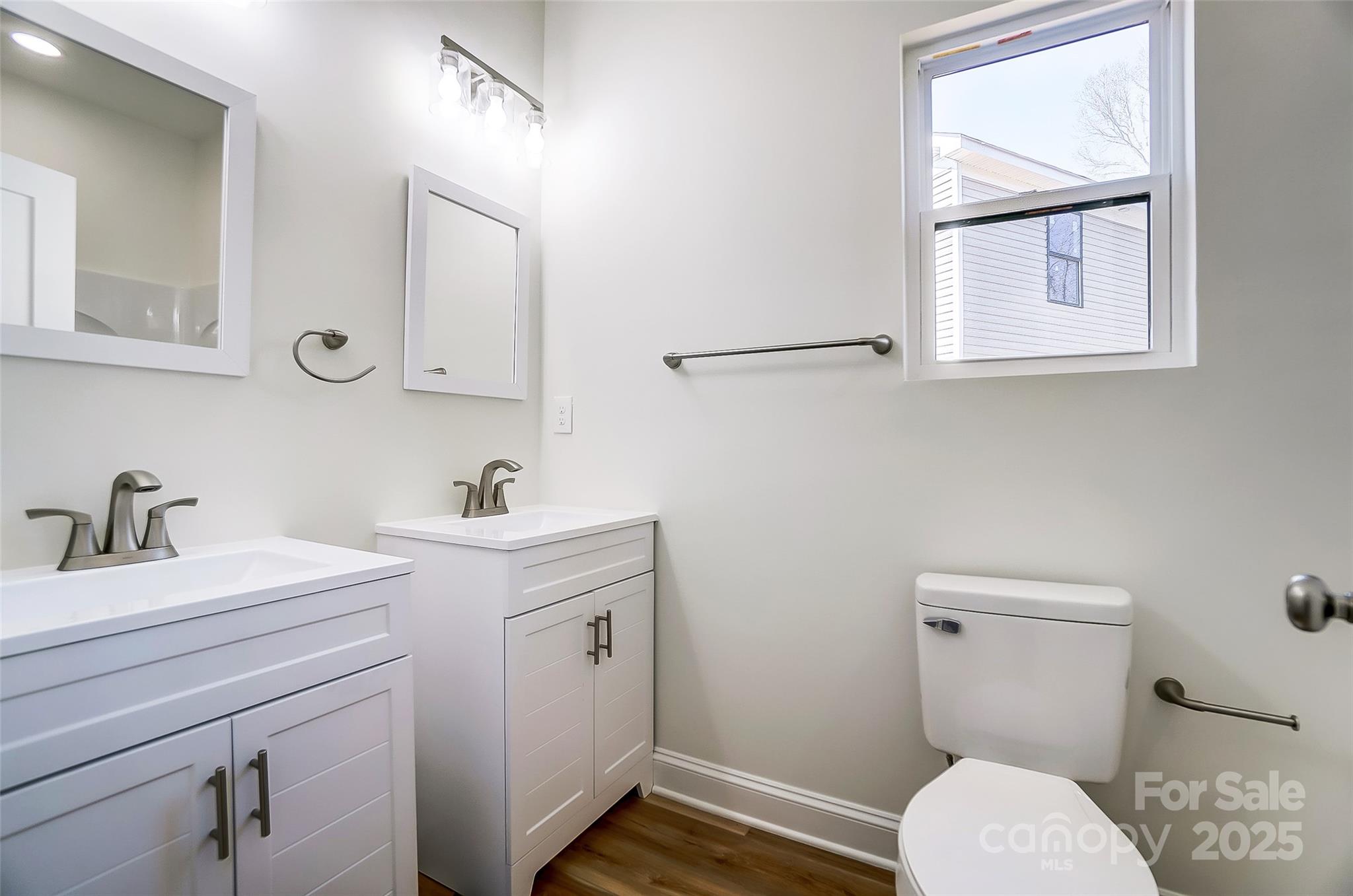 Bathroom with two white vanities, framed mirrors, wood-look flooring, and a window.