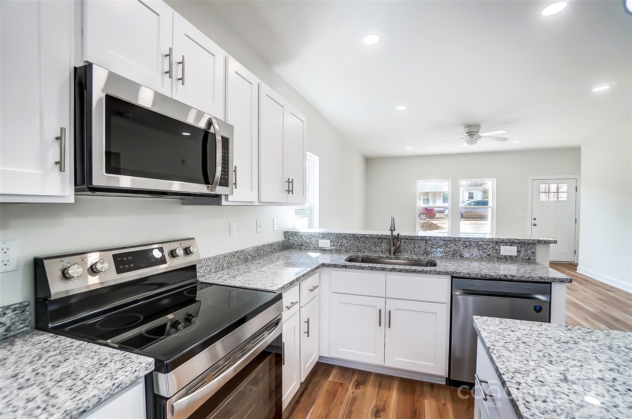 Kitchen with white cabinets, speckled granite counters, stainless steel appliances, and wood-look flooring.