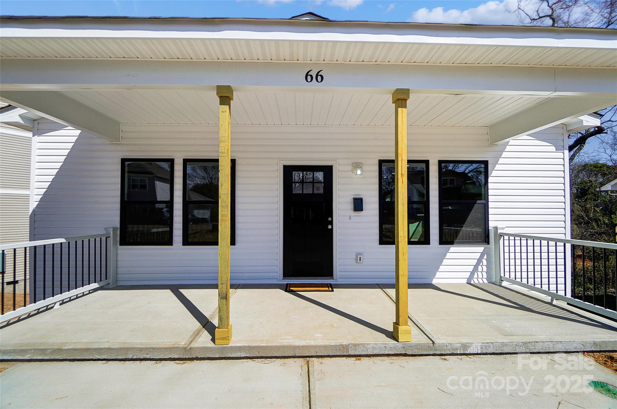 White house front porch with black door and windows, wooden posts, and the number 66.