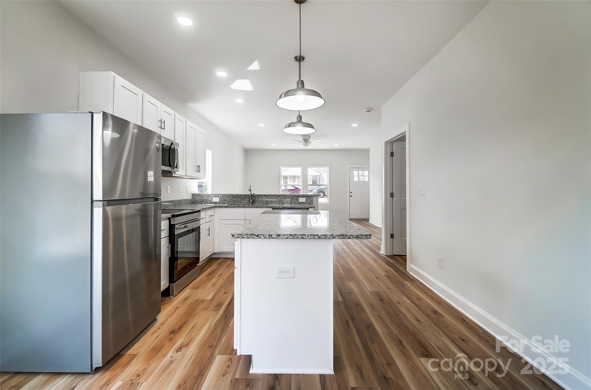 Kitchen with white cabinets, stainless steel appliances, granite island, and wood-look flooring.