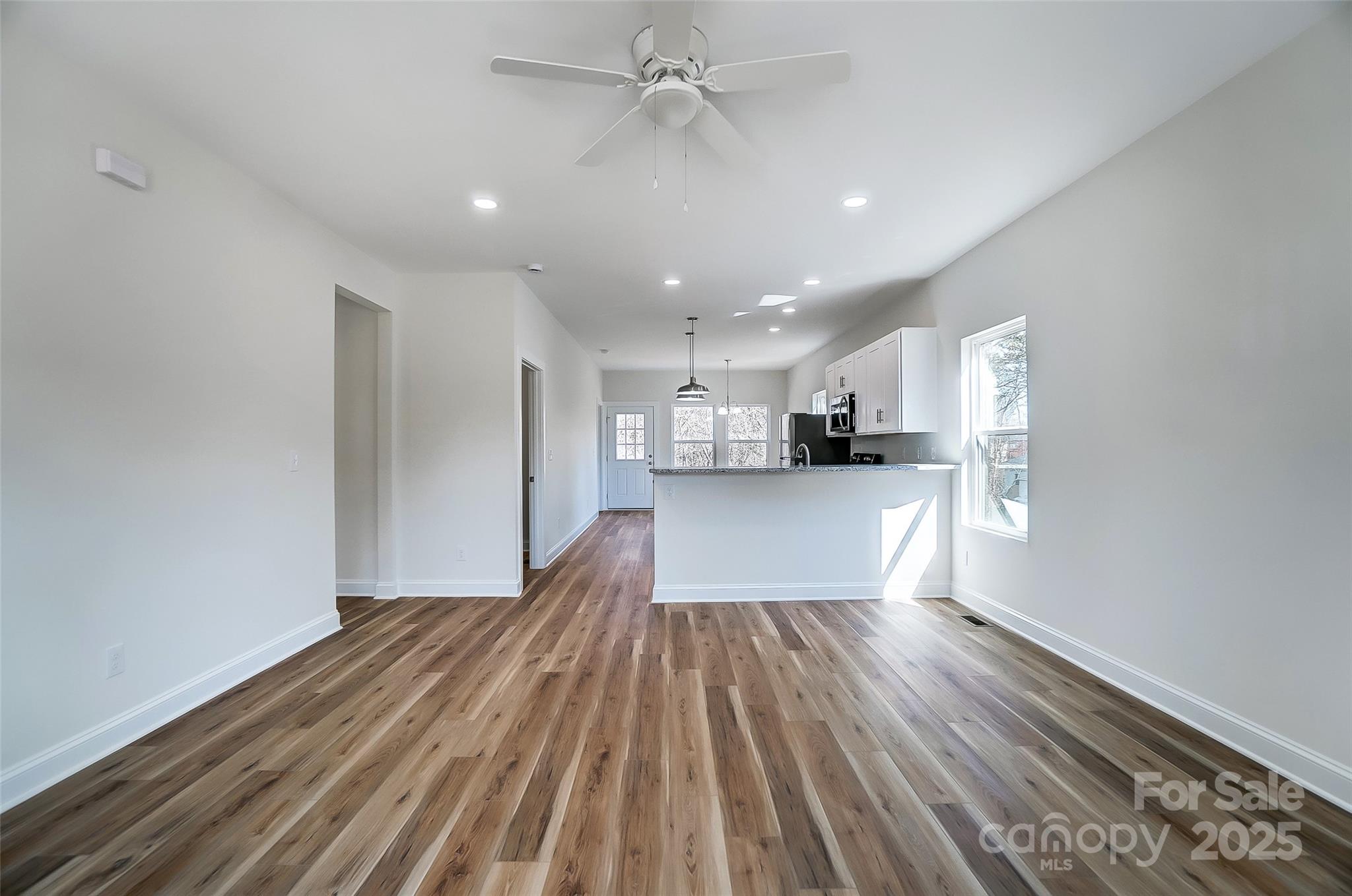 Open-plan living area with wood-look flooring and a kitchen peninsula with white cabinets.