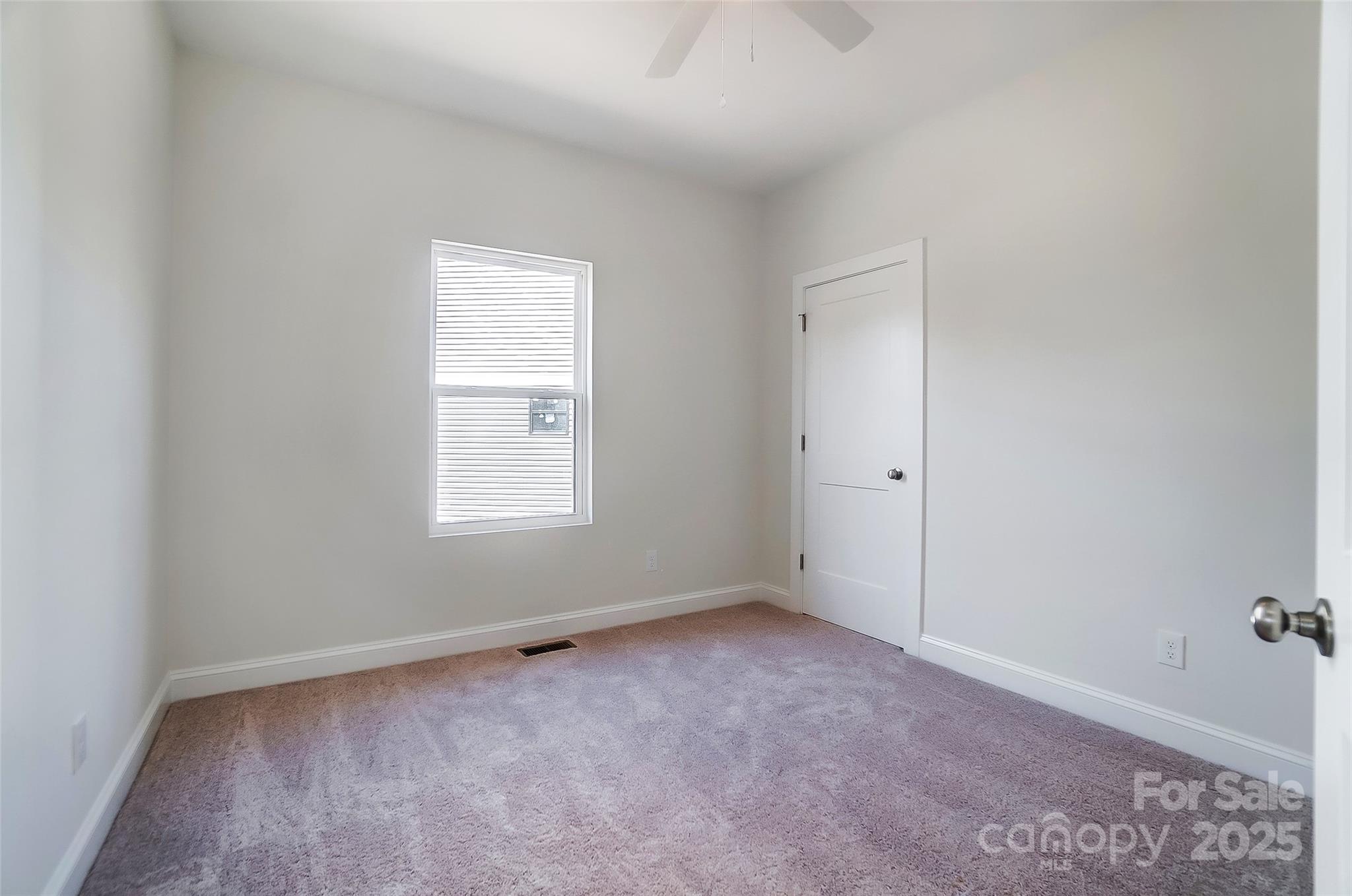 Empty bedroom with mauve carpet, a window with closed blinds, and a white door.