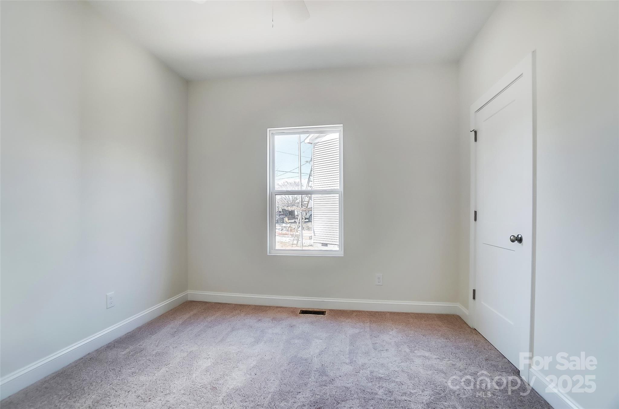 Empty bedroom with pale carpet, a centered window, and a closed white door.