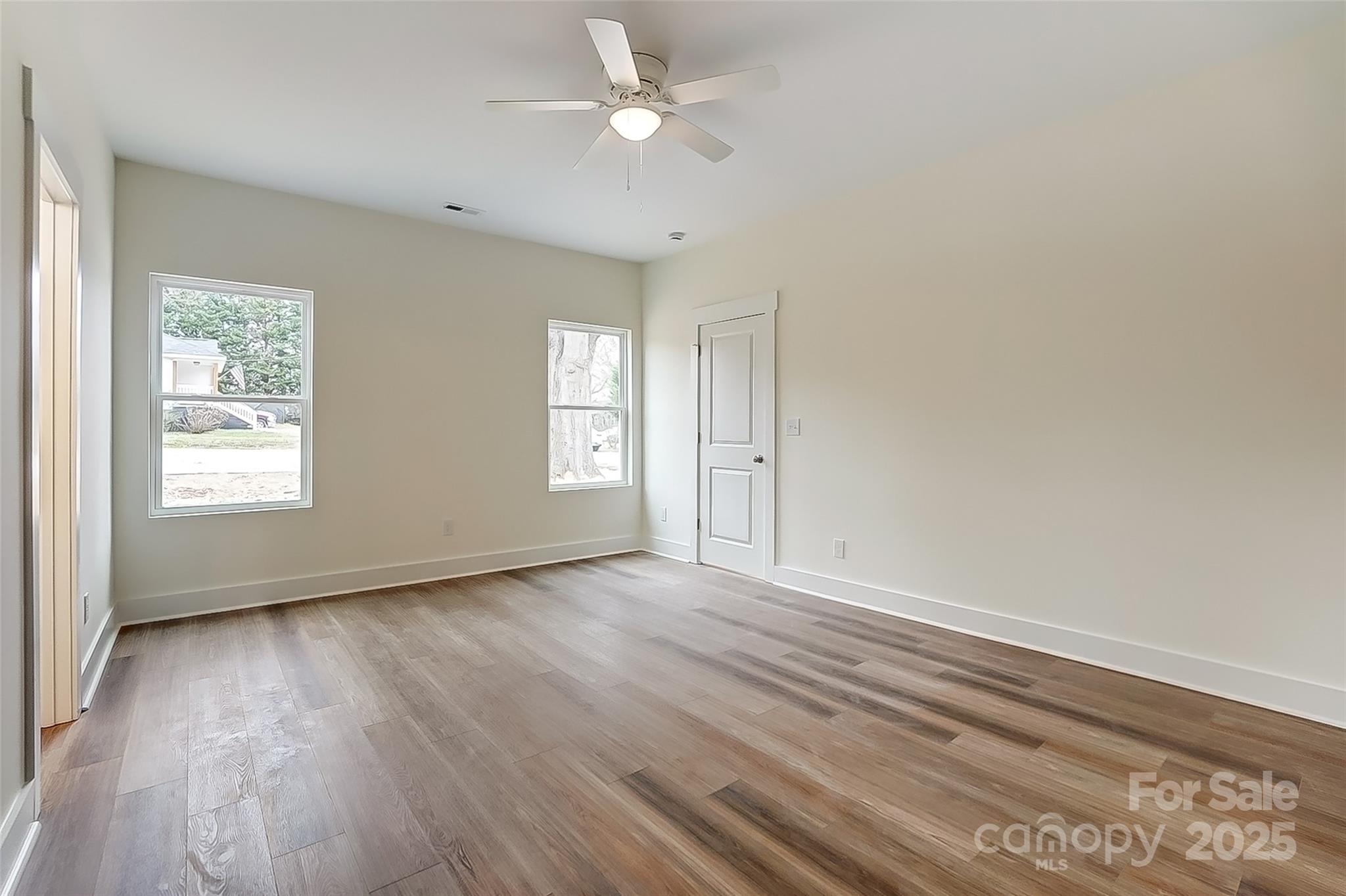 Empty room with wood-look flooring, two windows, a white door, and a ceiling fan.
