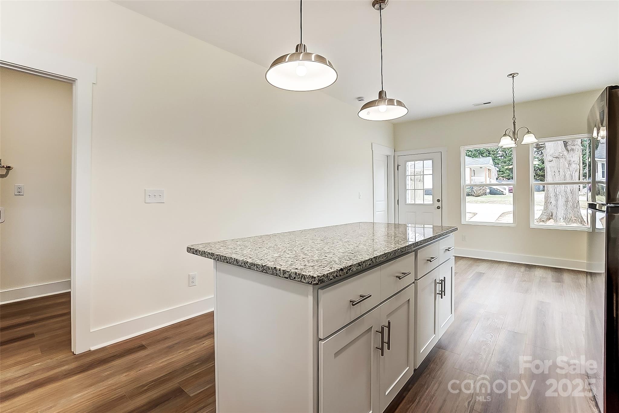 Kitchen with a large granite-topped island, pendant lights, and windows beside the exterior door.