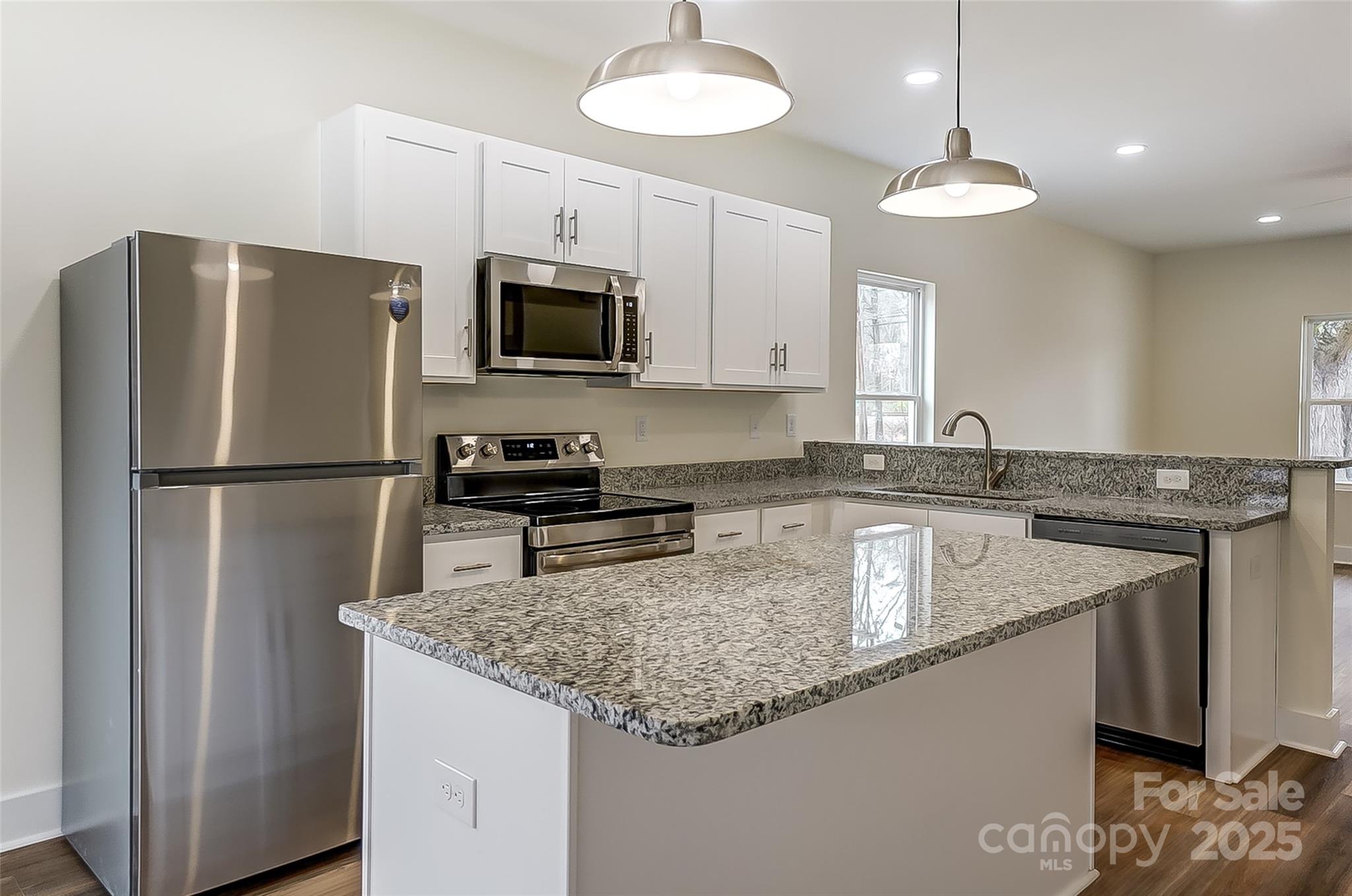 Kitchen with white cabinets, stainless steel appliances, and a large granite island.