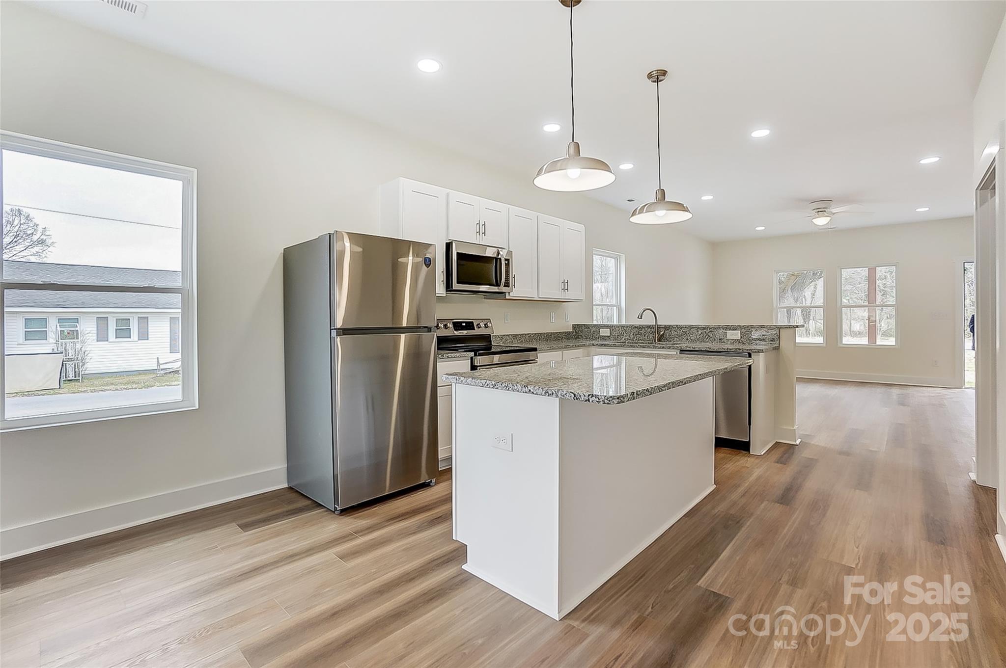 Bright kitchen with stainless steel appliances, granite island, white cabinets, and wood-look flooring.
