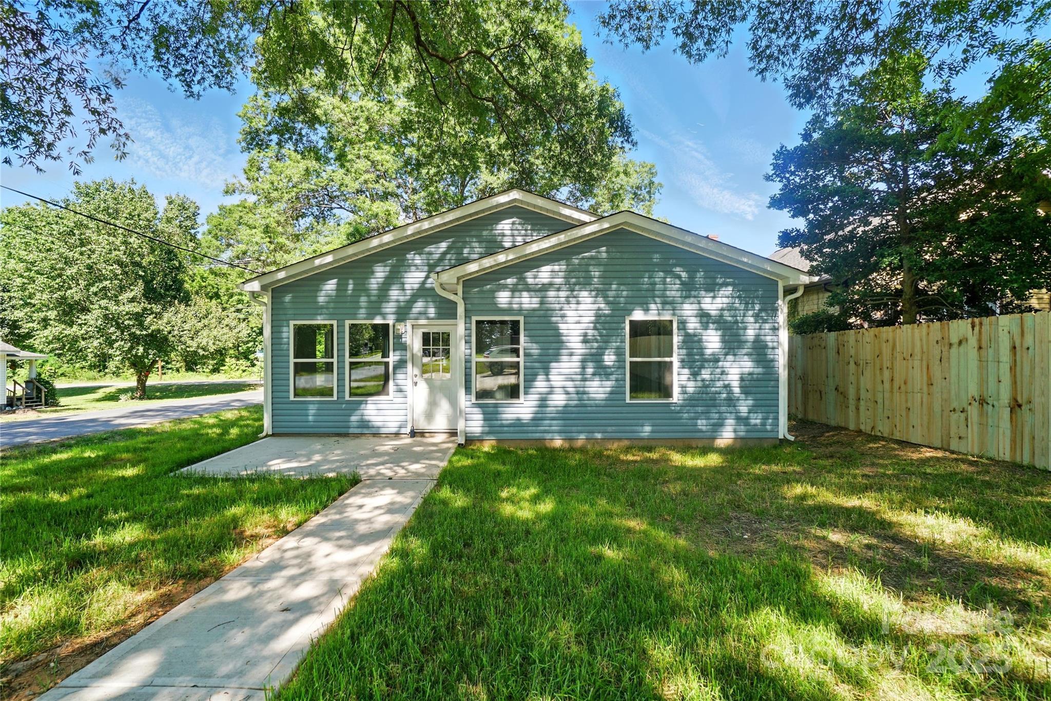 Blue-gray house with white trim, a concrete walkway, grassy yard, and wooden fence.