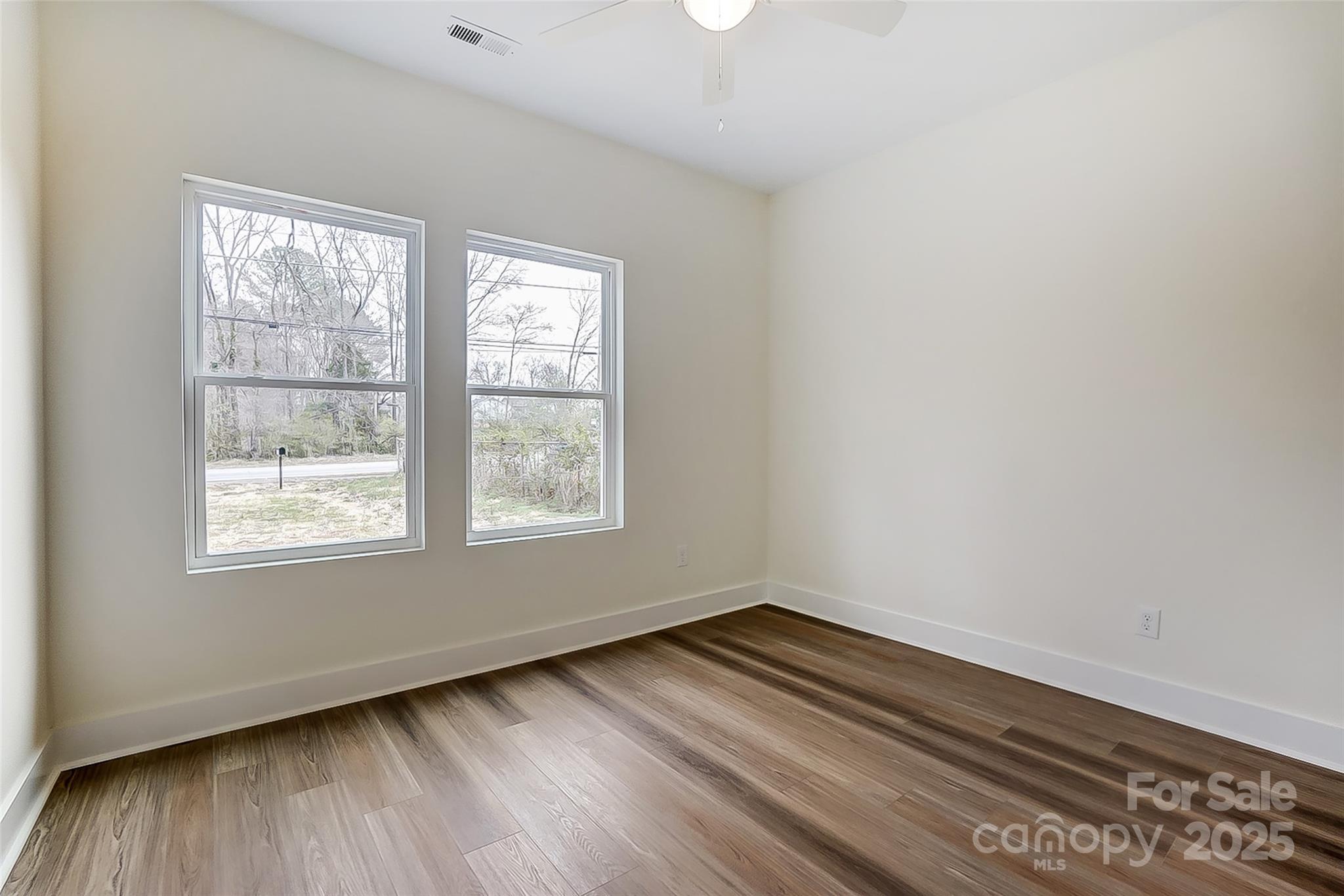 Empty room with wood-look flooring, two windows, and a ceiling fan.