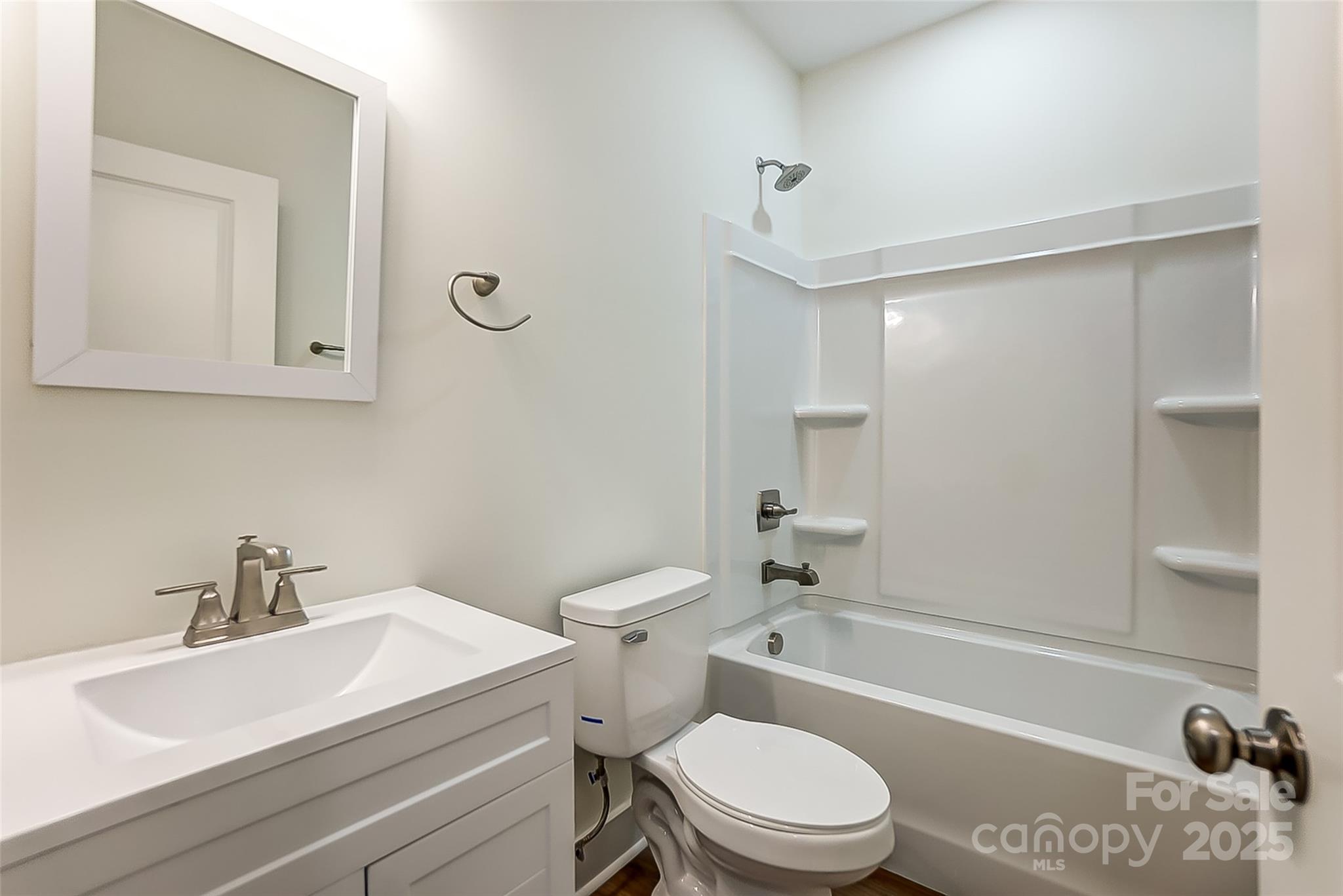 Bathroom with white vanity, toilet, and bathtub with built-in shower shelves.