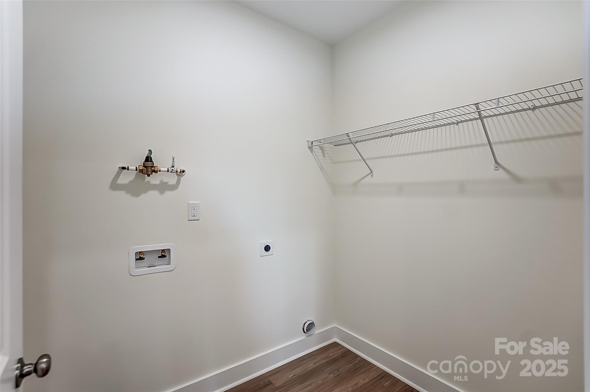 Empty laundry room with washer and dryer hookups and a long wire shelf.