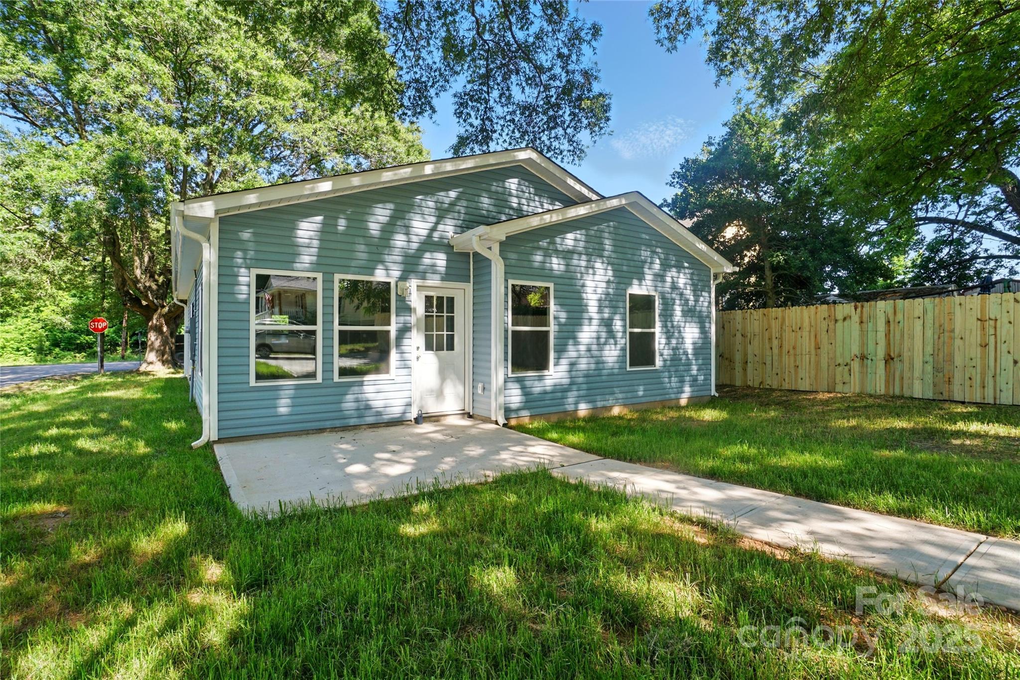 Blue-gray house with white trim, concrete walkway, grassy yard, and wooden fence.