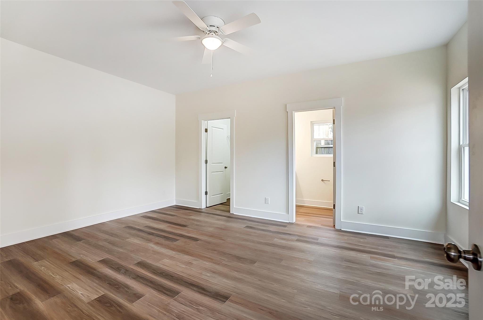 Empty bedroom with wood-look flooring, a ceiling fan, and two open doorways.