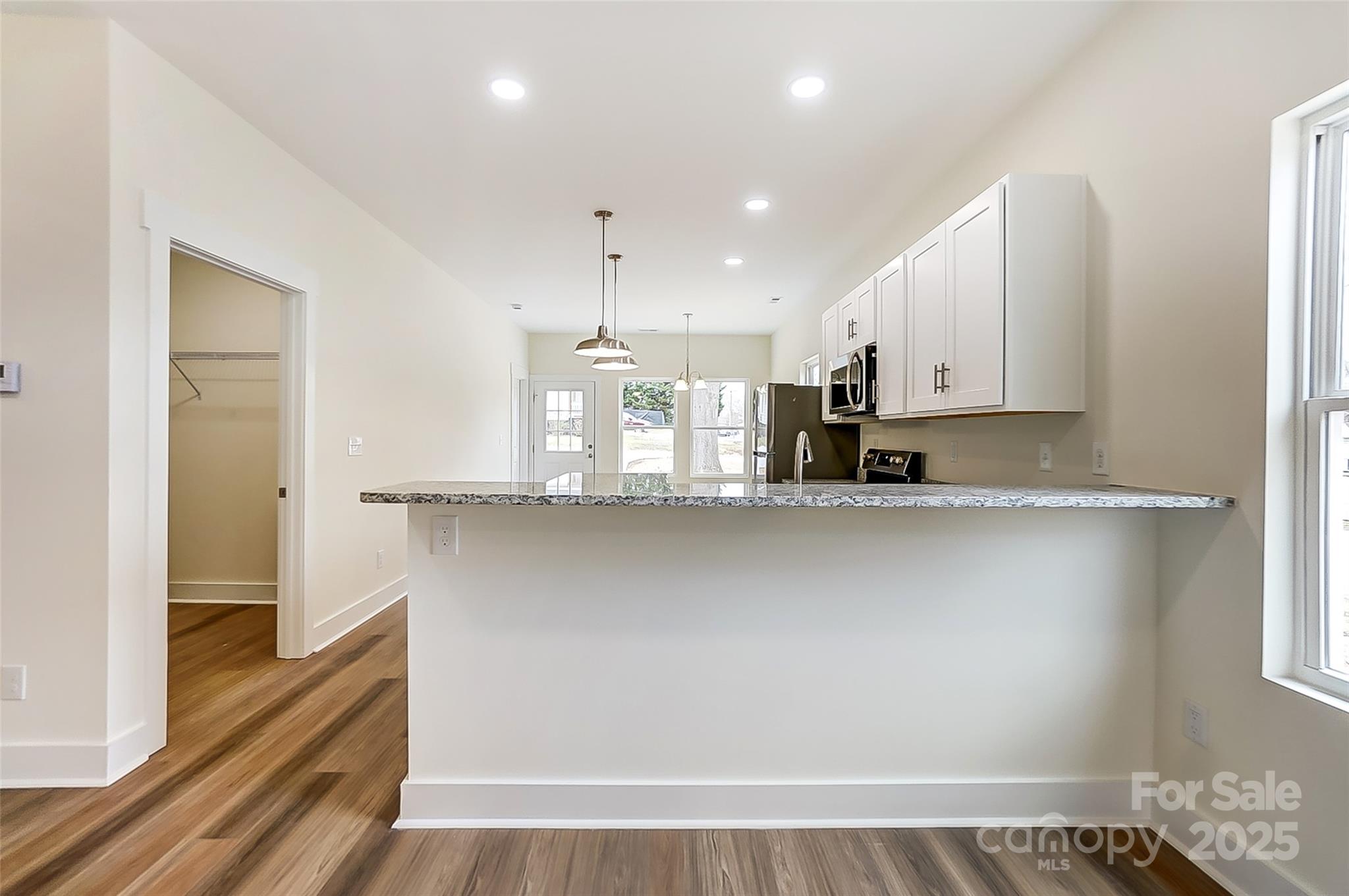 Bright kitchen with white cabinets, a long granite breakfast bar, stainless appliances, and wood-look floors.