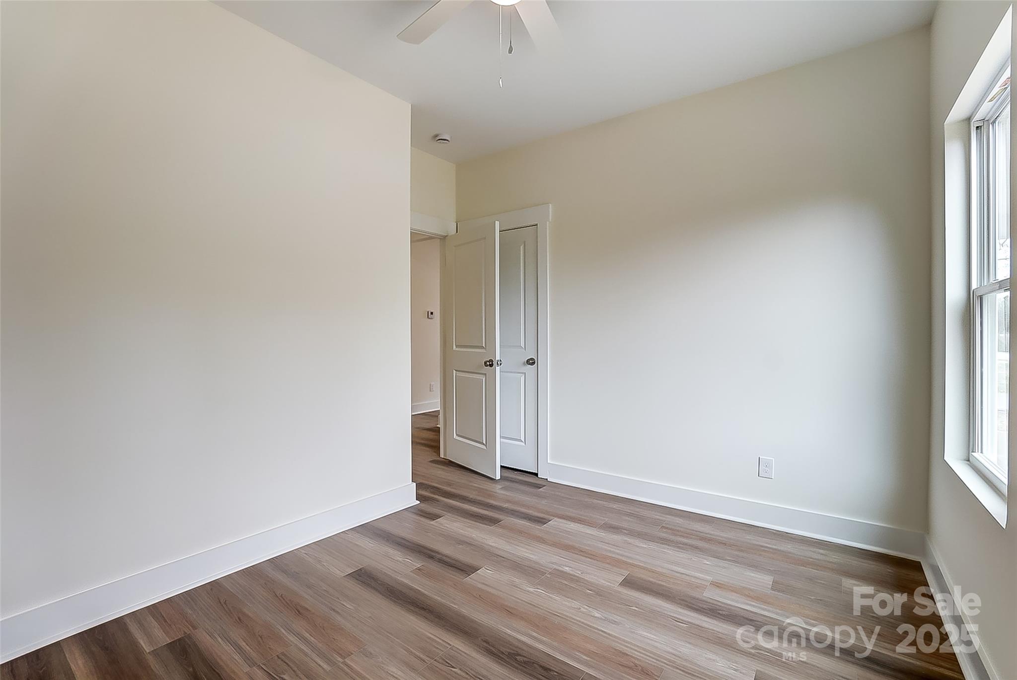 Empty bedroom with wood-look flooring, ceiling fan, and a tall window.