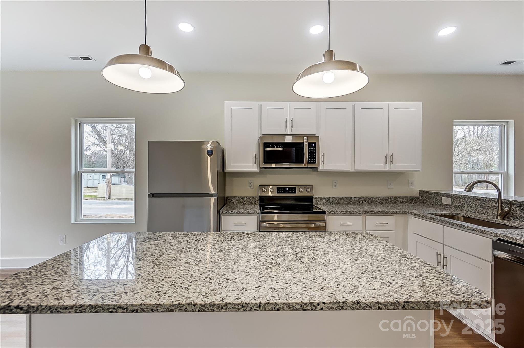 Kitchen with white cabinets, stainless steel appliances, speckled granite counters, and a large island.