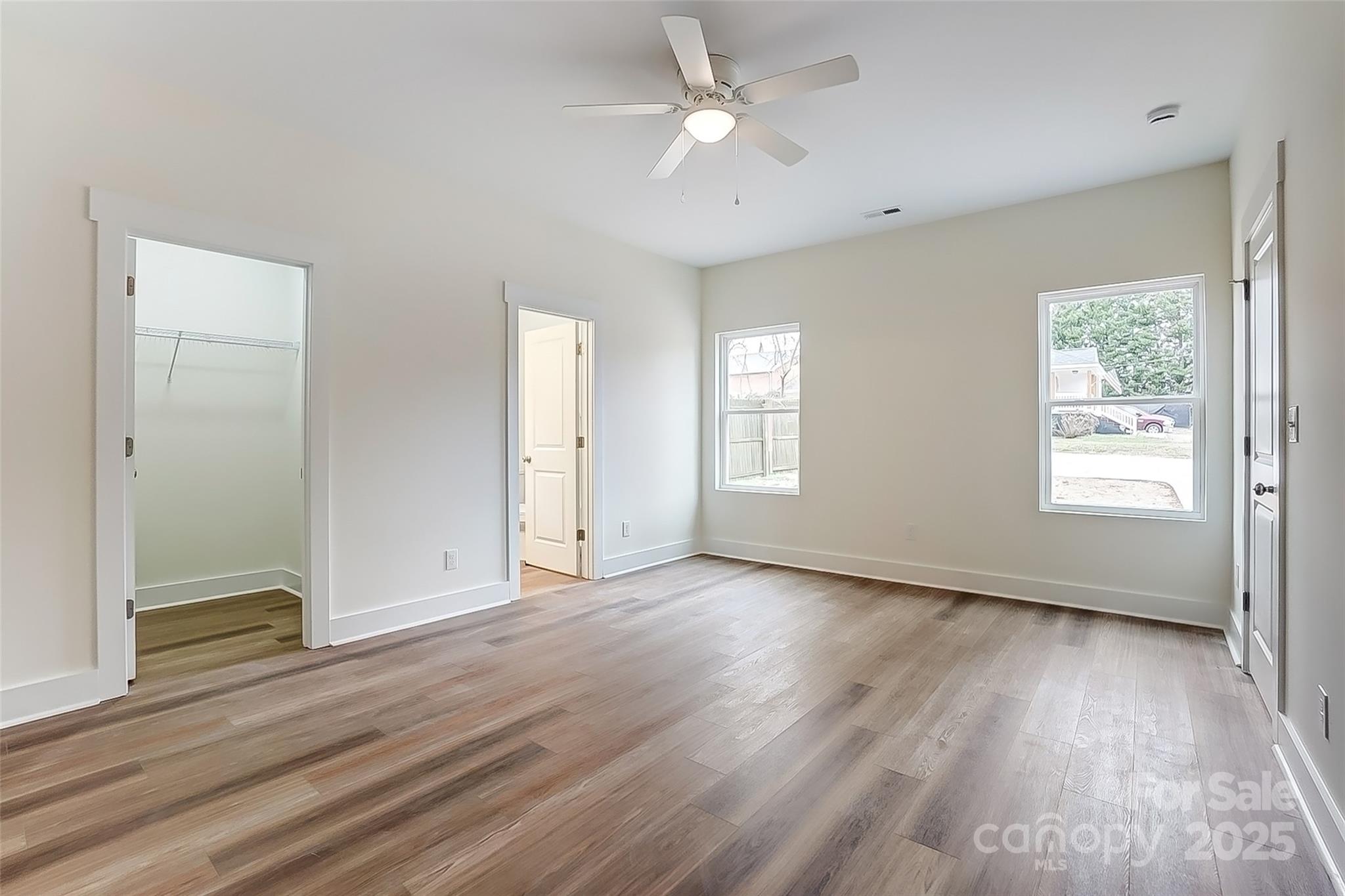 Vacant bedroom with wide-plank wood flooring, a ceiling fan, and an open closet.
