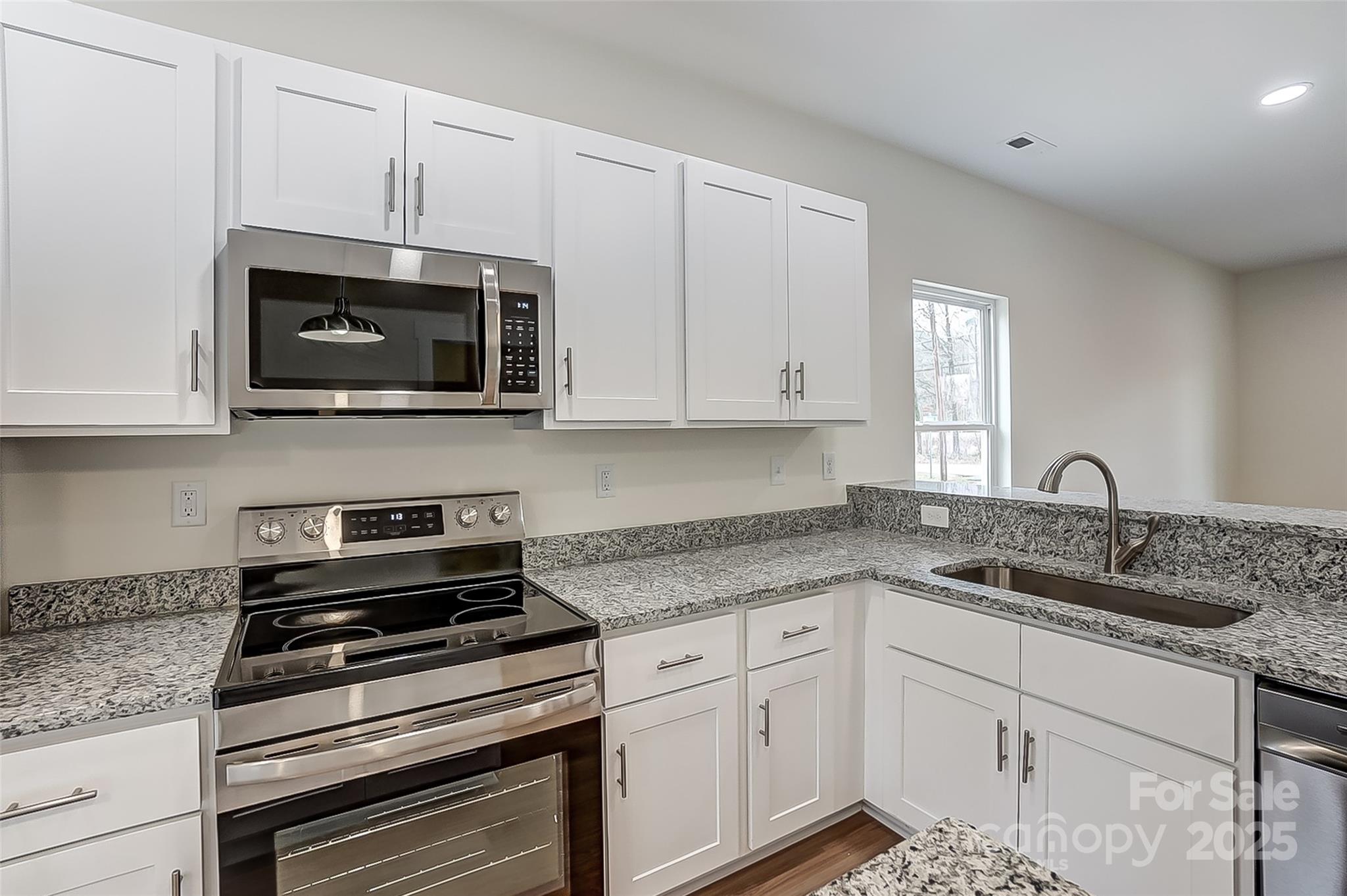 Kitchen with white cabinets, granite counters, stainless appliances, and a sink beneath the window.