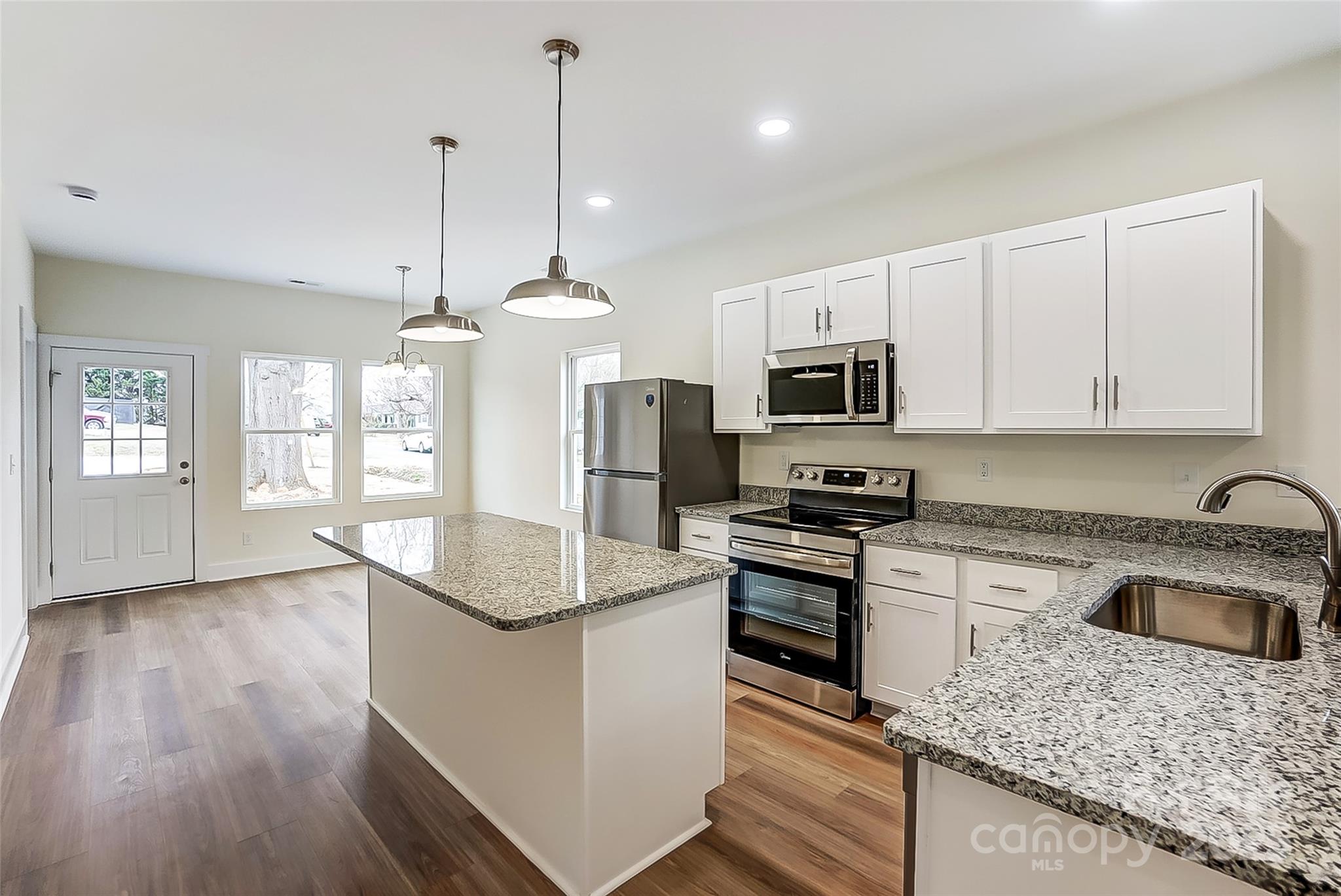 Vacant kitchen with a large granite island, white cabinets, and stainless steel appliances.