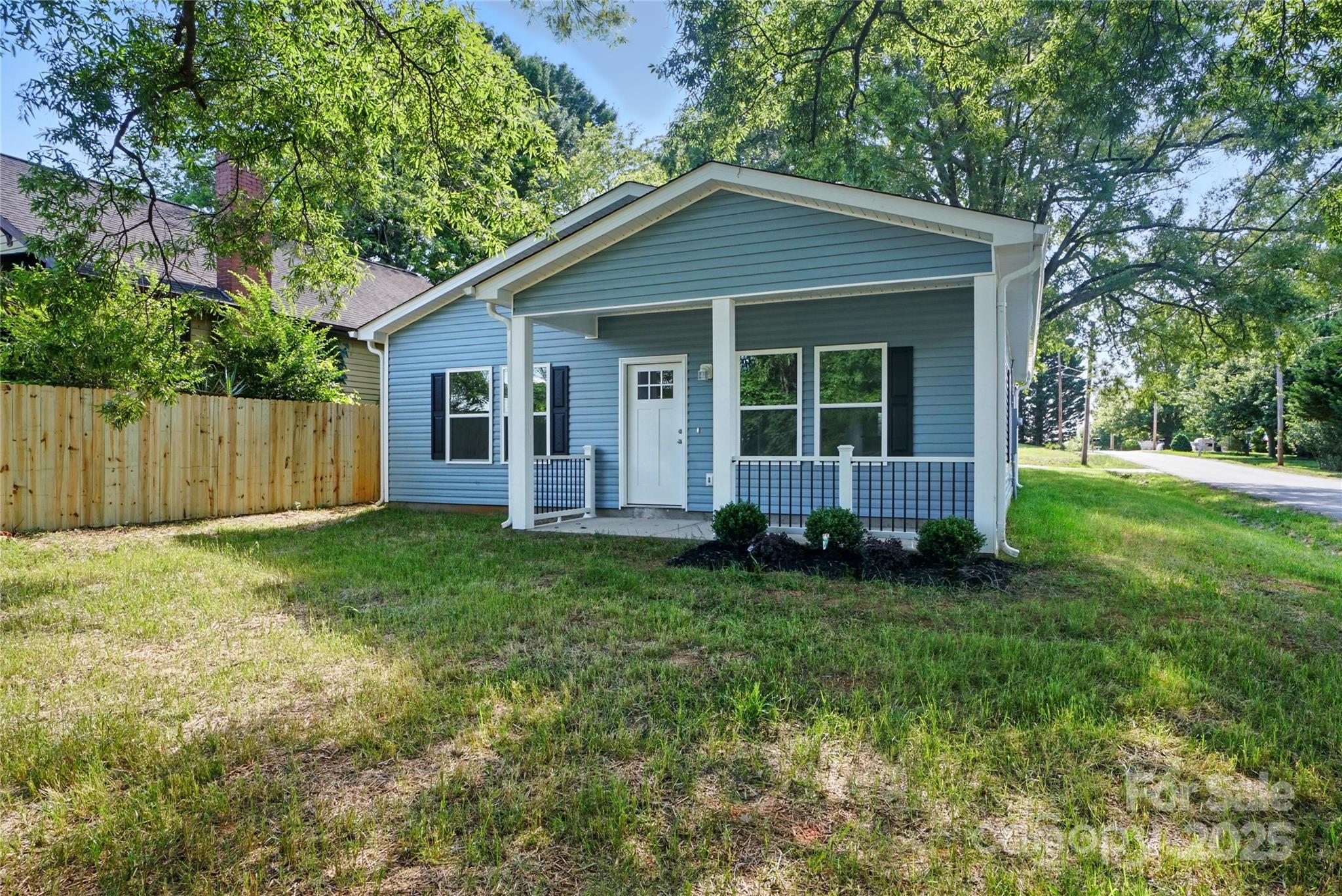 Blue house with a white covered porch, black railings, and a shady grassy yard.