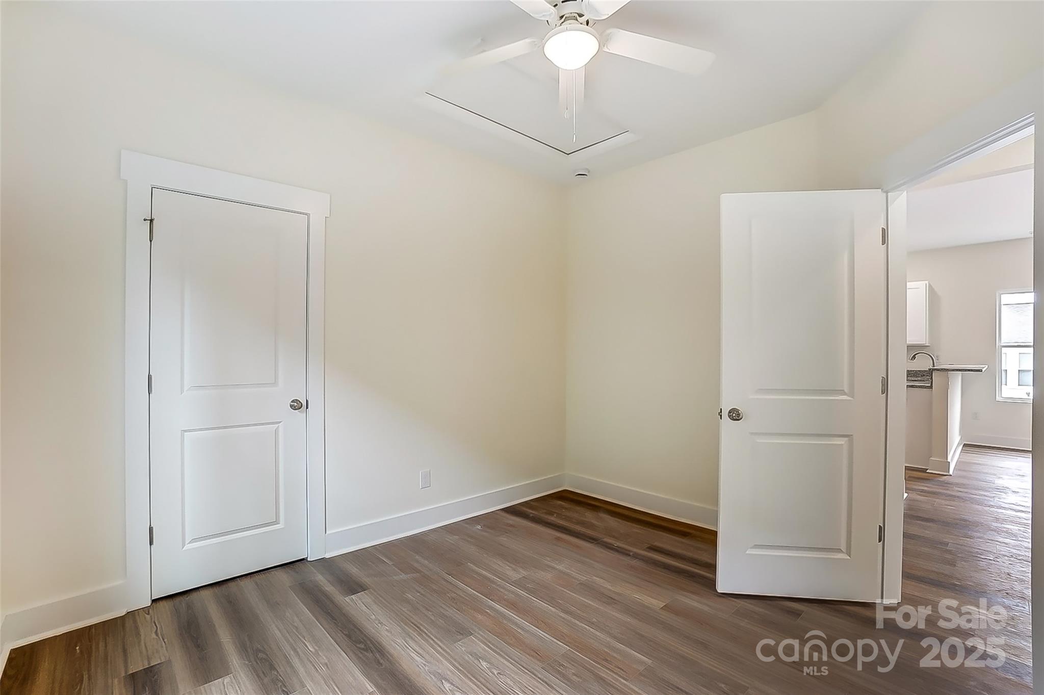 Empty room with dark wood-look flooring, a ceiling fan, and an open doorway to a sink area.