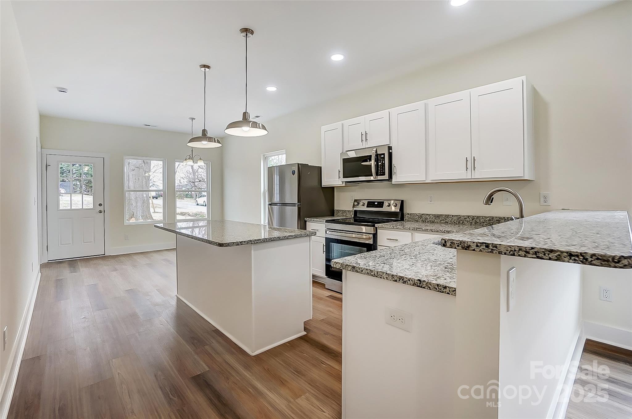 Vacant kitchen with white cabinets, stainless steel appliances, granite counters, a central island, and breakfast bar.