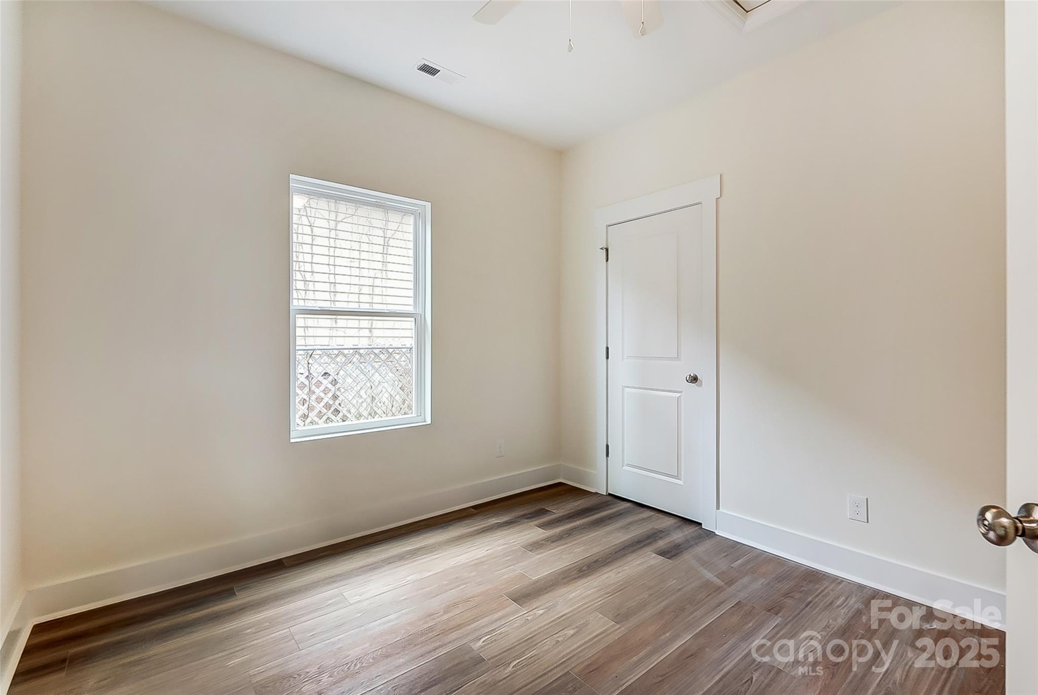 Empty room with wood-look plank flooring, a window, and a white paneled door.