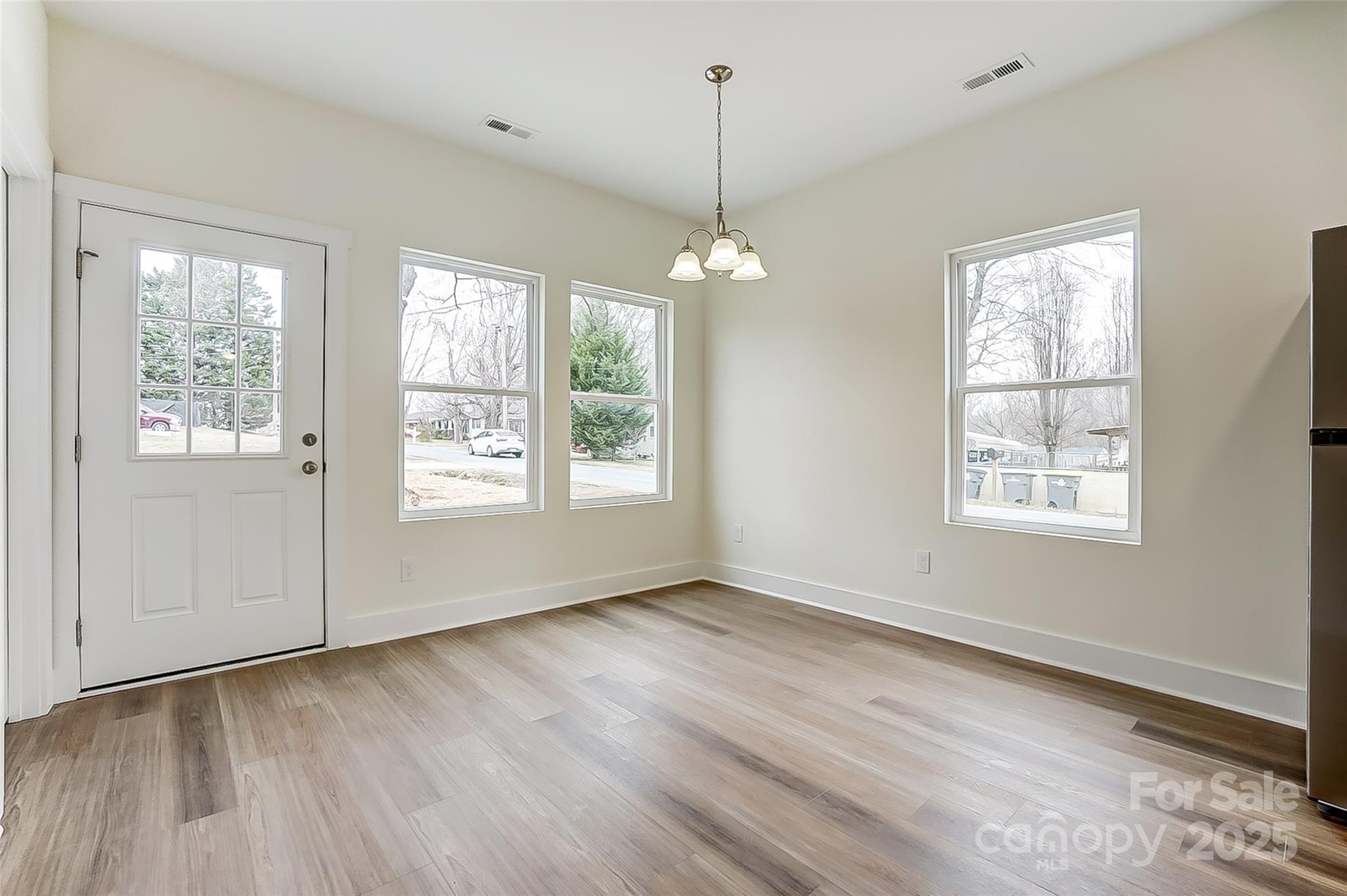 Empty room with wood-look flooring, a glass-paneled exterior door, three windows, and a chandelier.