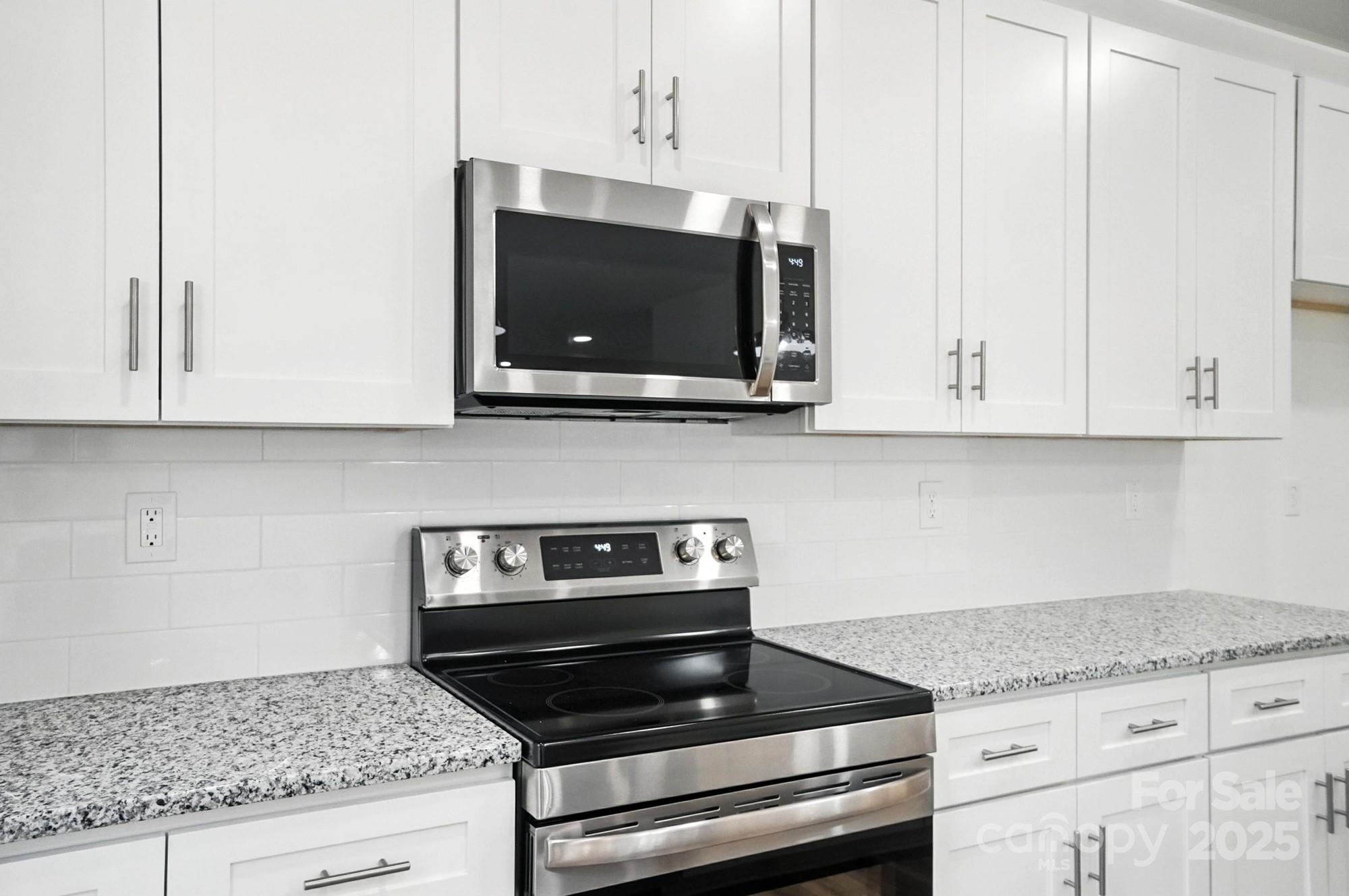 White kitchen with granite counters, stainless steel range, and over-the-range microwave.