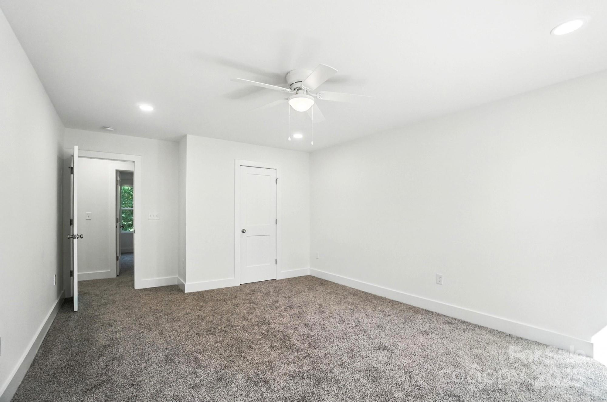 Empty bedroom with gray carpet, white walls, a ceiling fan, and an open doorway.
