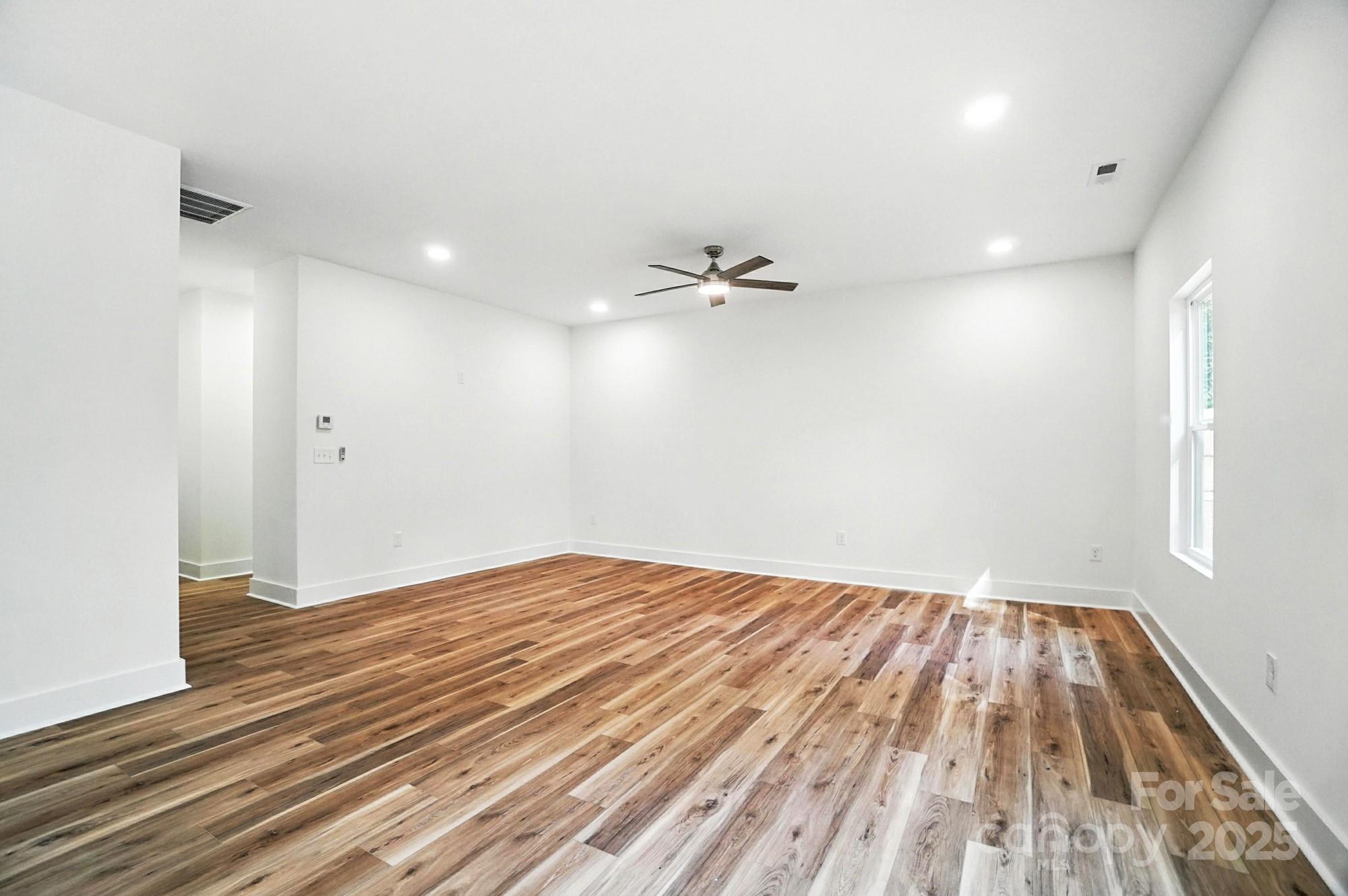 Empty living room with wide-plank wood floors, white walls, and a ceiling fan.