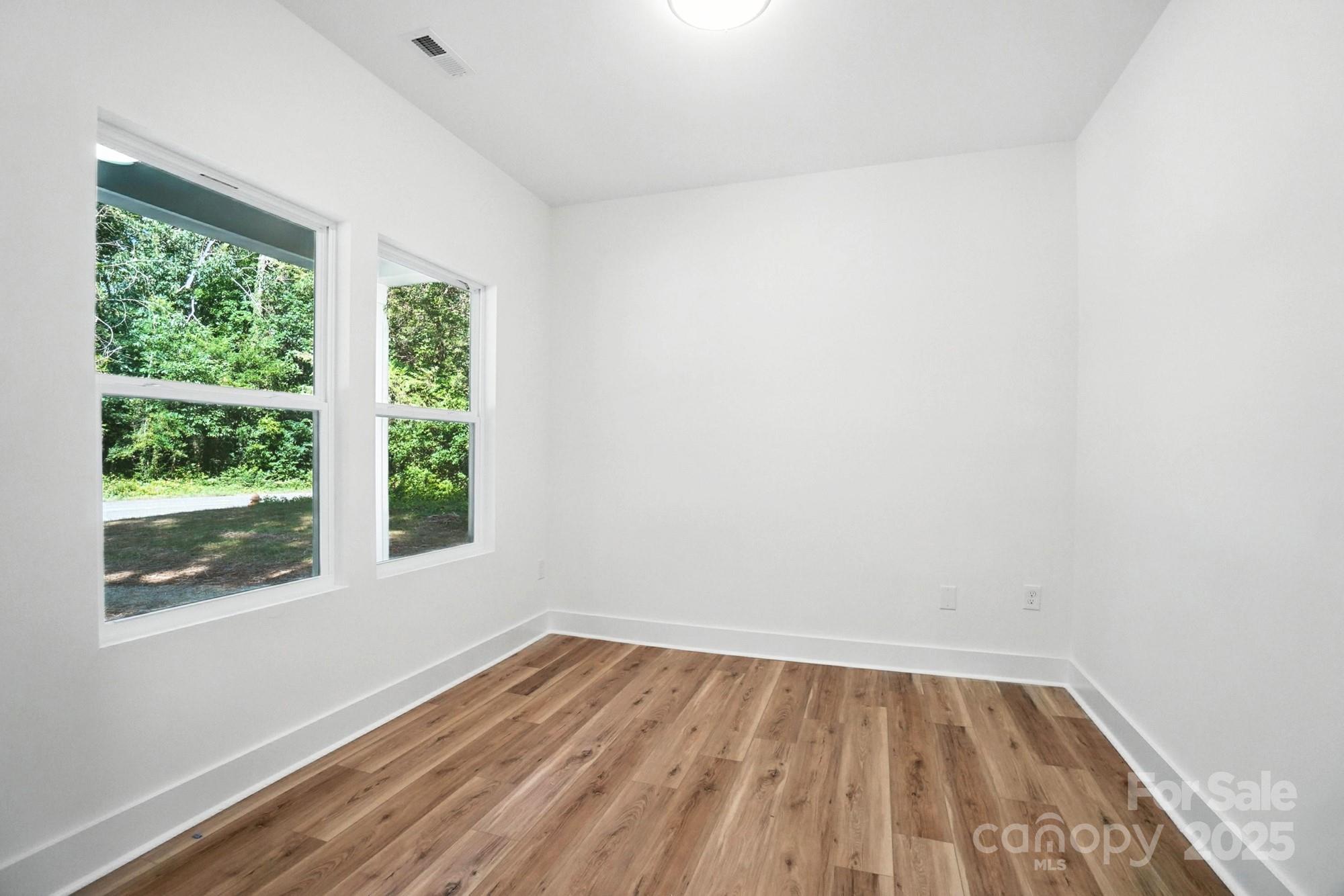 Vacant room with wood-look plank flooring and two windows overlooking trees.