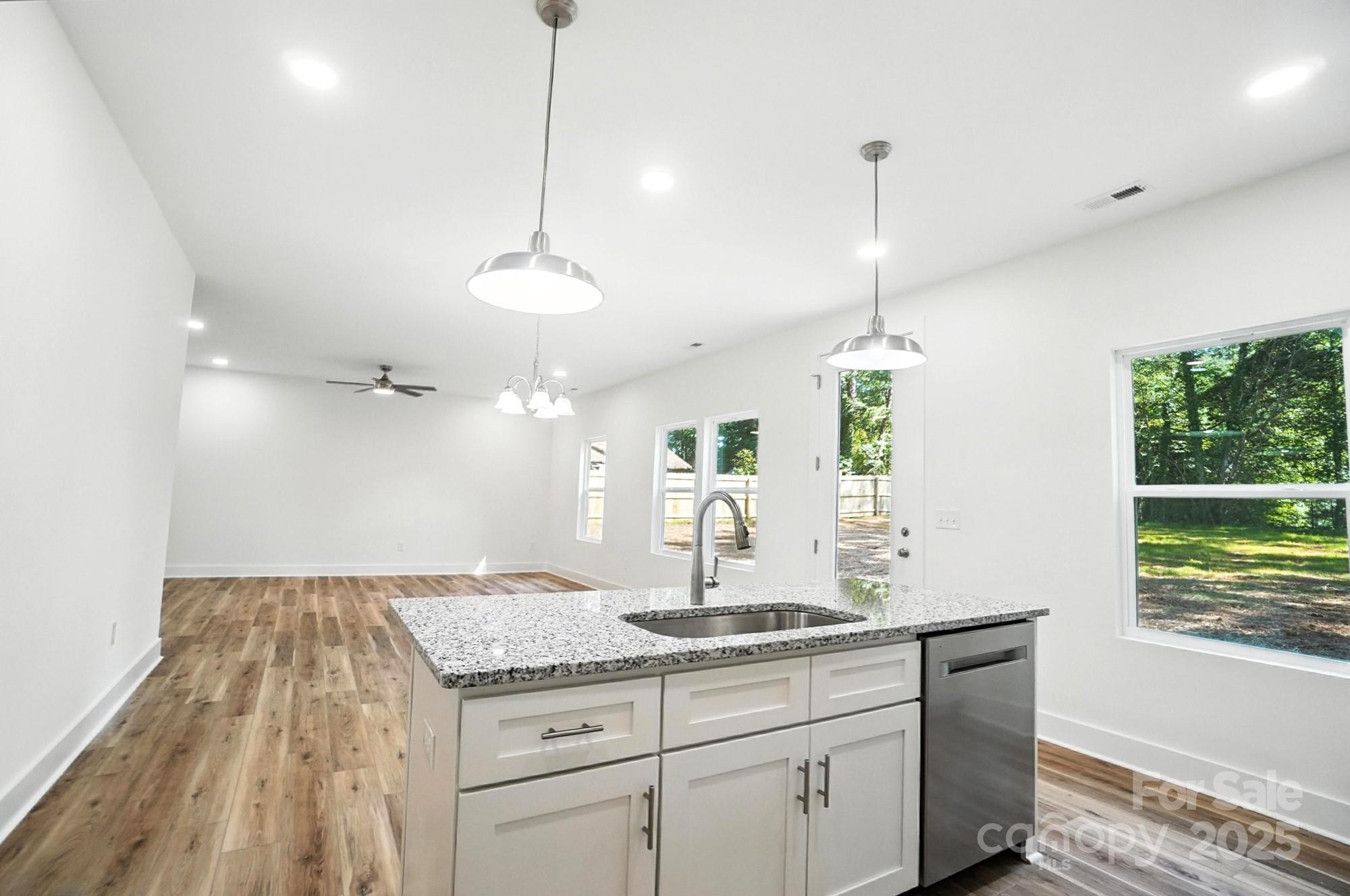 Bright vacant kitchen with granite island and sink, opening onto a wood-floored living area.