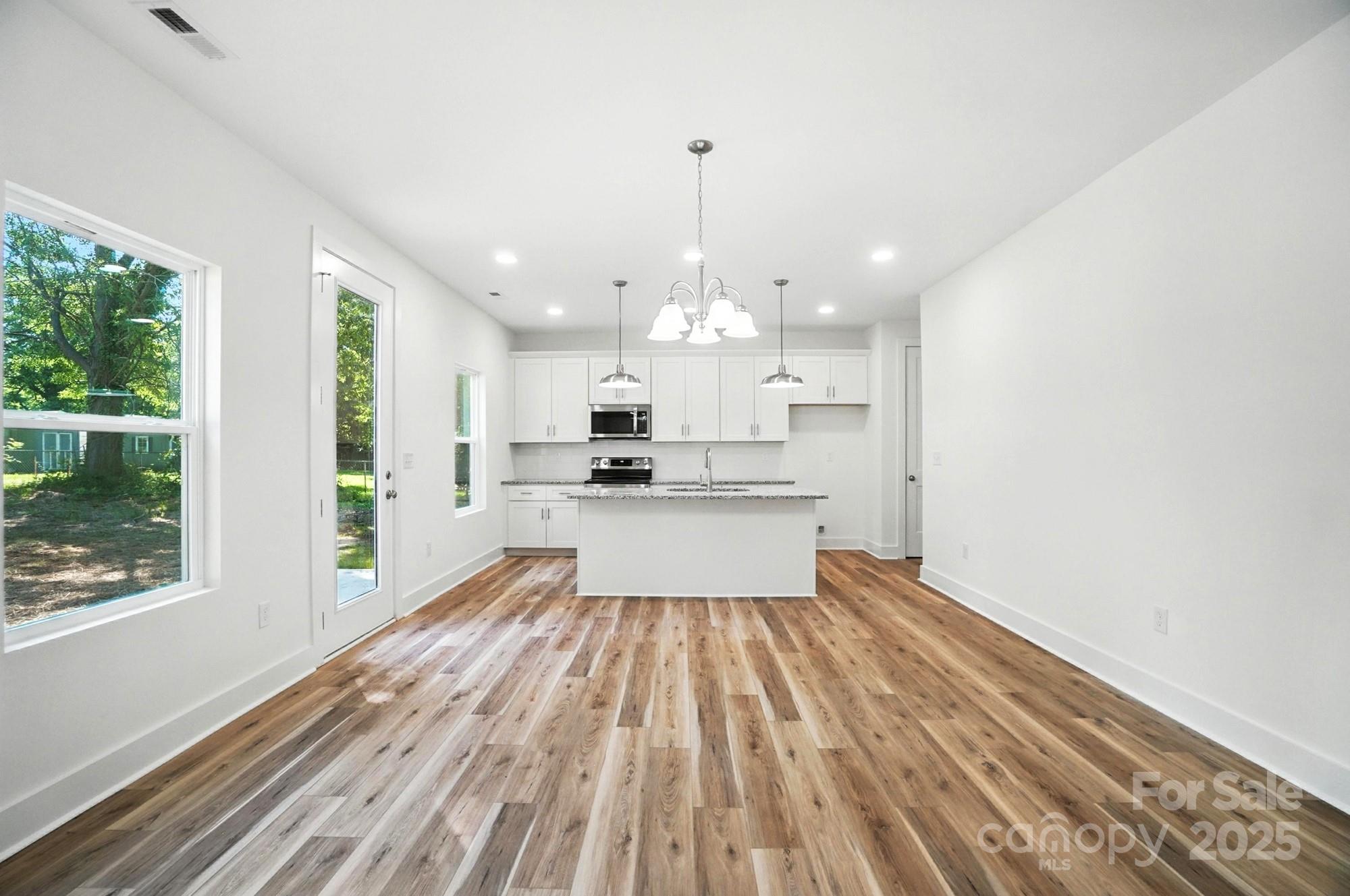 Bright vacant kitchen with white cabinets, granite island, stainless steel appliances, and wood-look floors.