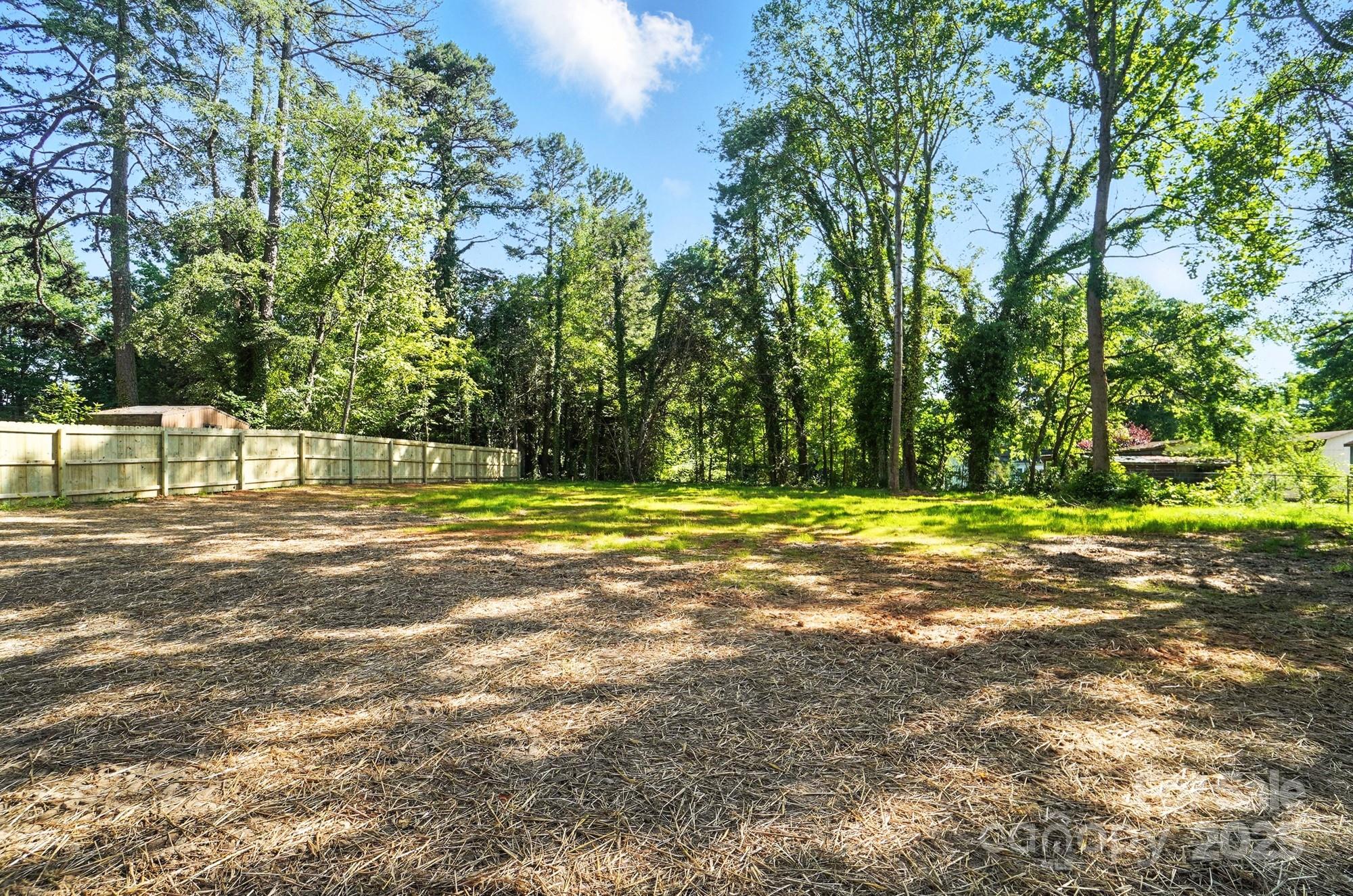 Spacious tree-lined backyard with a wooden privacy fence and straw-covered ground.