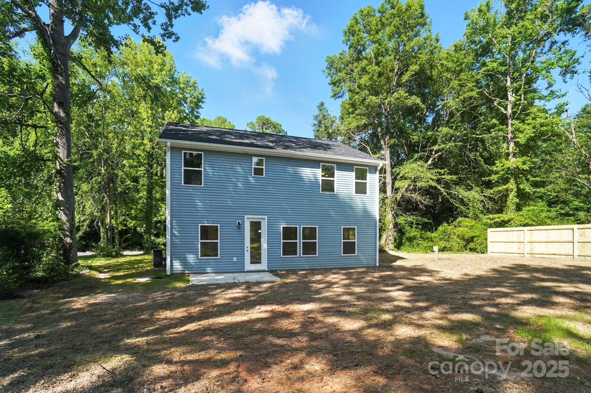 Rear of a blue two-story house with white trim, a bare yard, and a wooded setting.