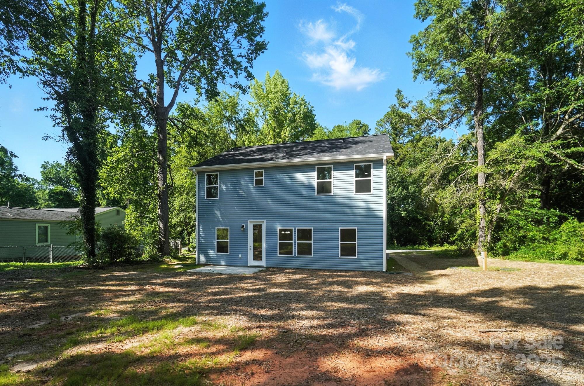 Rear of a two-story blue house with white trim, set among mature trees beside a broad, mostly bare yard.
