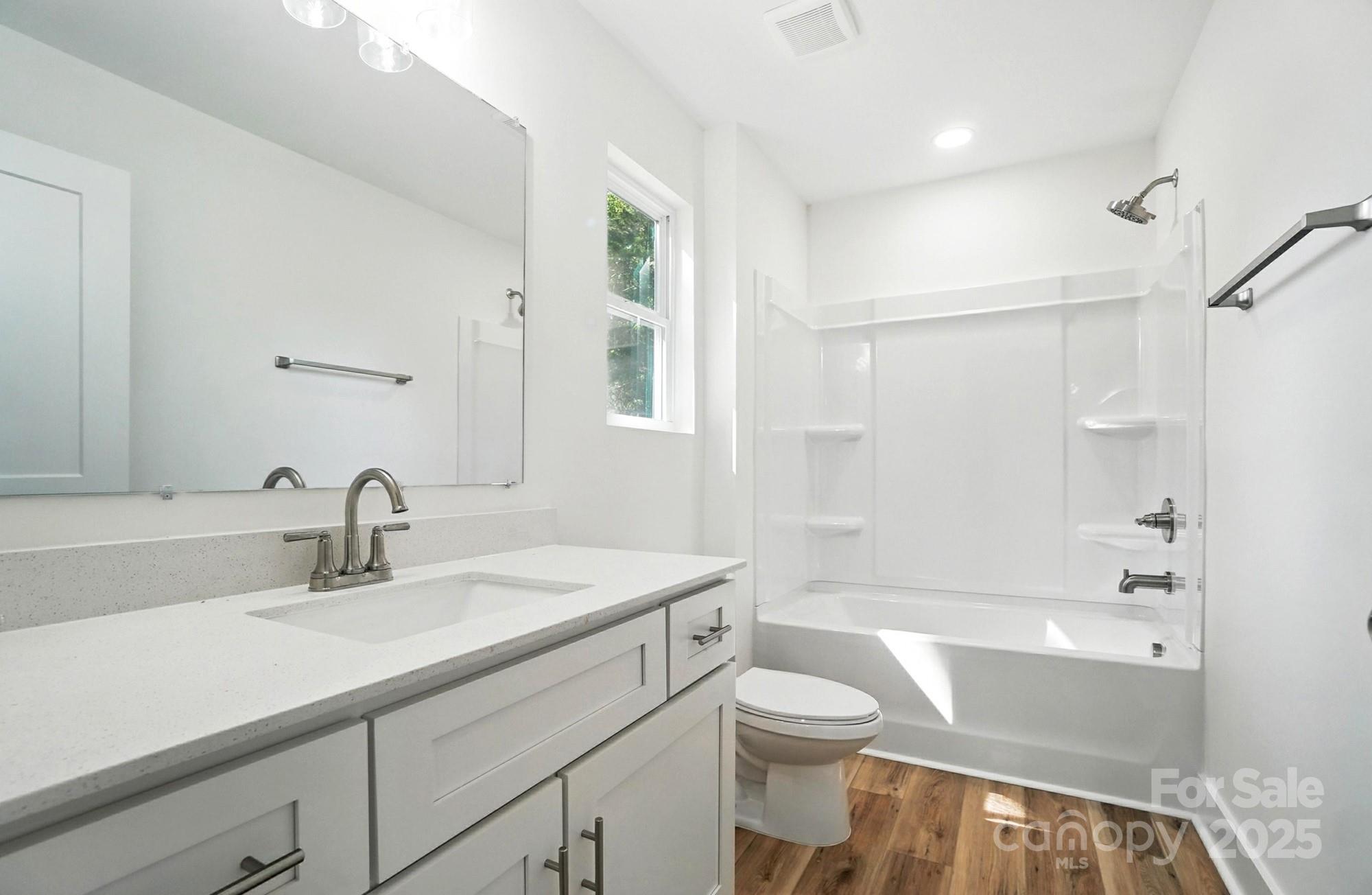 Bright white bathroom with a long vanity, tub and shower, window, and wood-look floor.