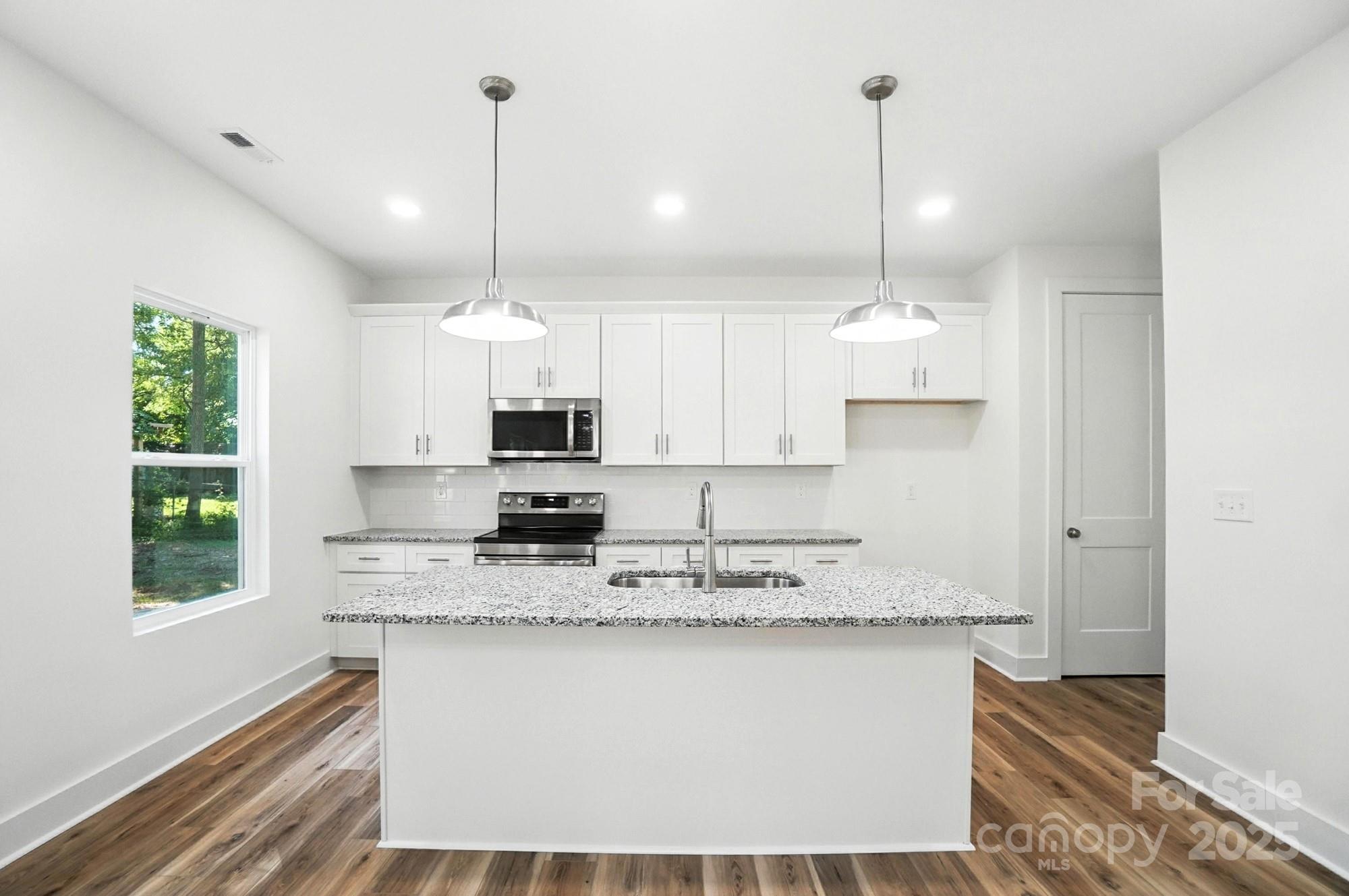 Bright white kitchen with a granite island, stainless steel appliances, and warm wood floors.