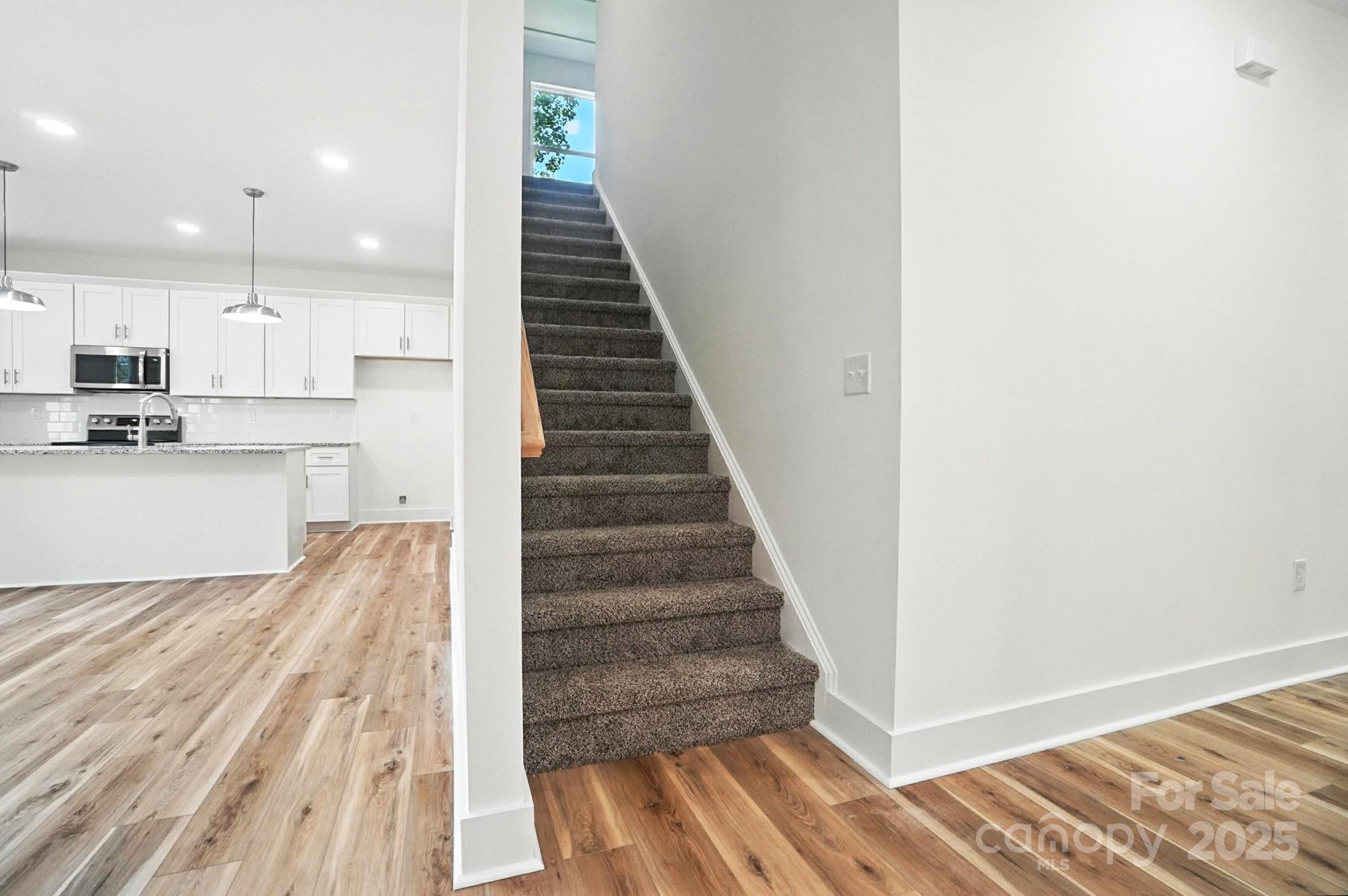 Open kitchen beside a carpeted staircase, with white cabinets and wood-look floors.