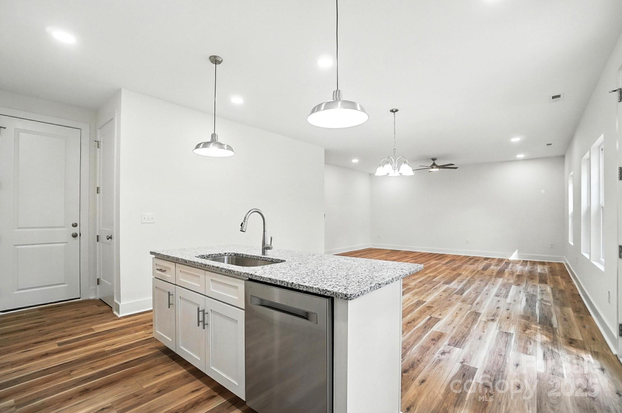 Kitchen island with granite countertop and stainless dishwasher opens to a vacant living area.