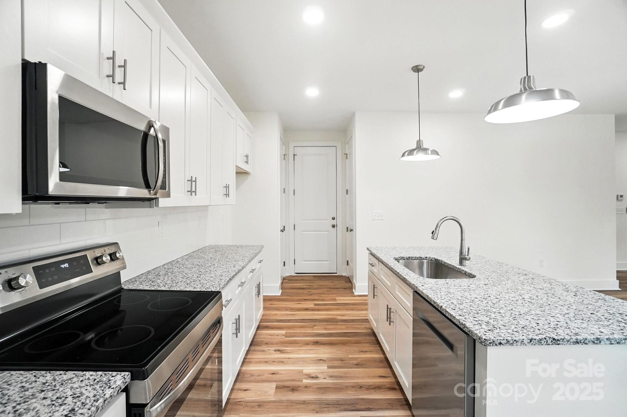 Modern kitchen with white cabinetry, granite counters, stainless steel appliances, and warm wood floors.
