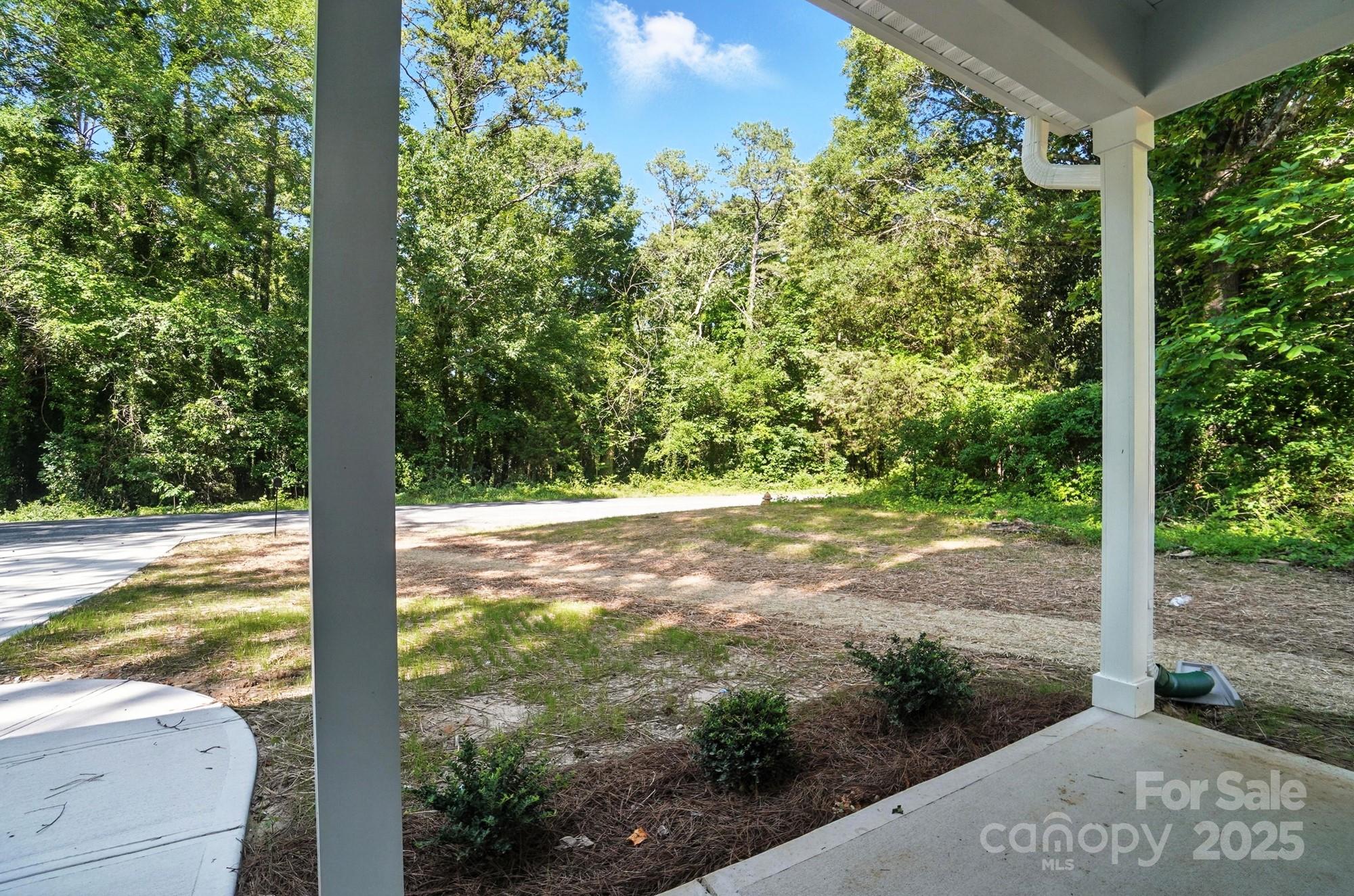 Covered porch overlooks a yard, driveway, and dense wooded tree line.