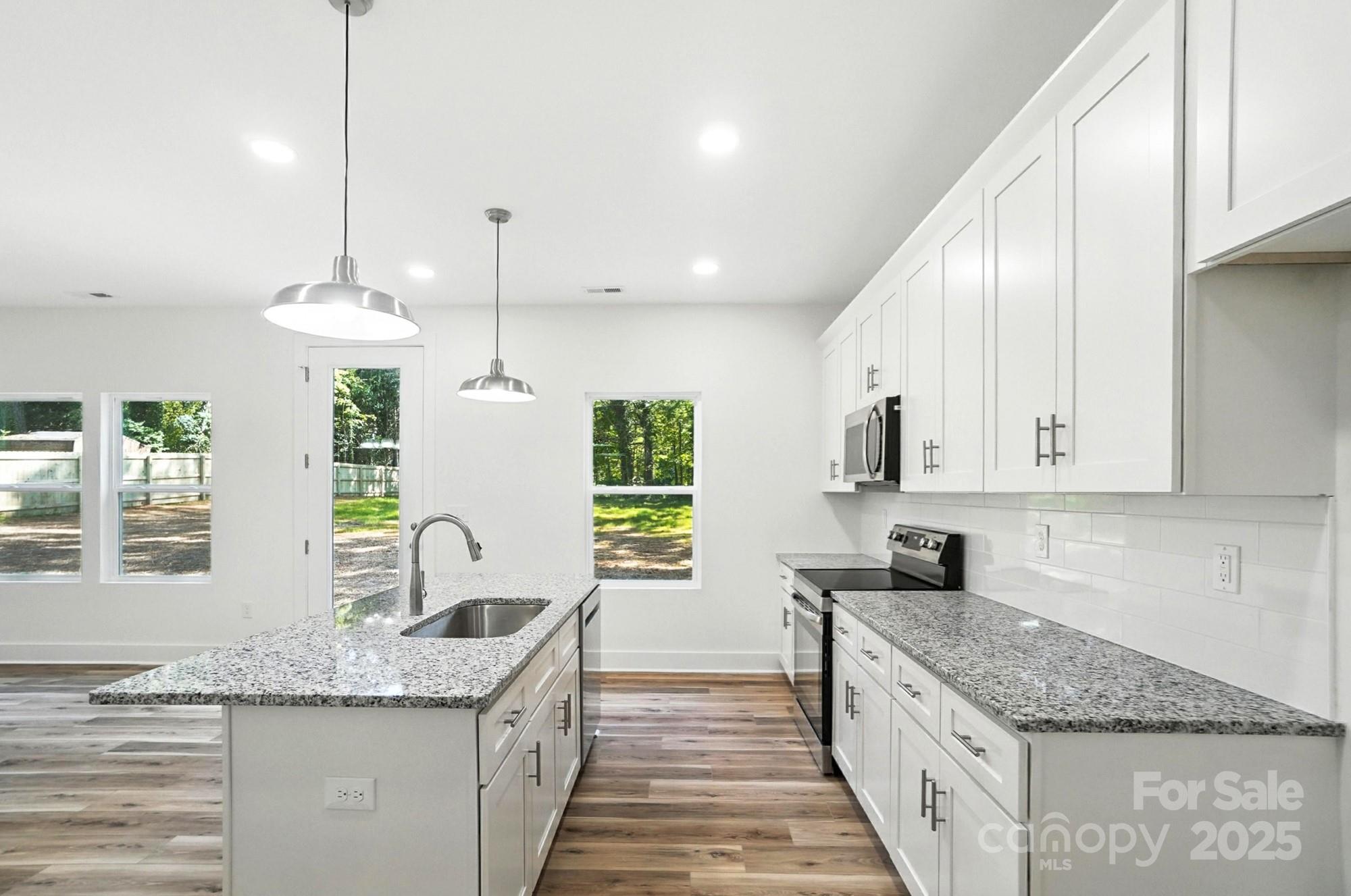 Bright kitchen with white cabinets, granite counters, a large island, and stainless steel appliances.