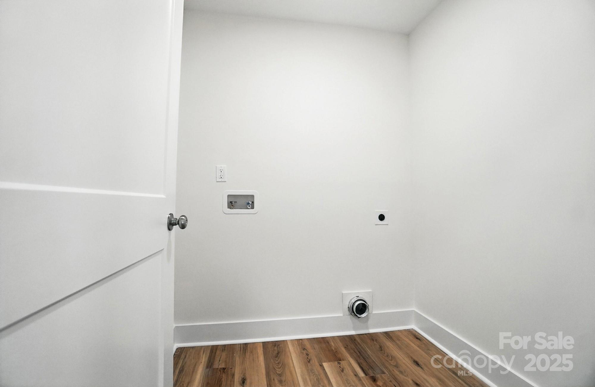 Empty laundry area with washer hookups, drain, and wood-look flooring.