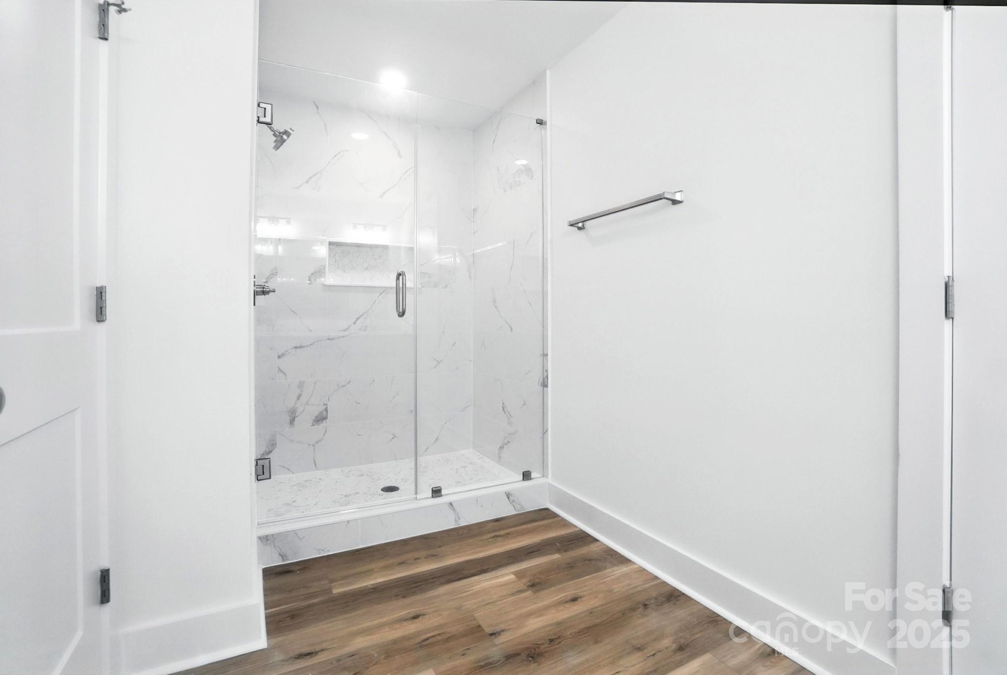 Modern bathroom with a marble-look walk-in shower and wood-look flooring.