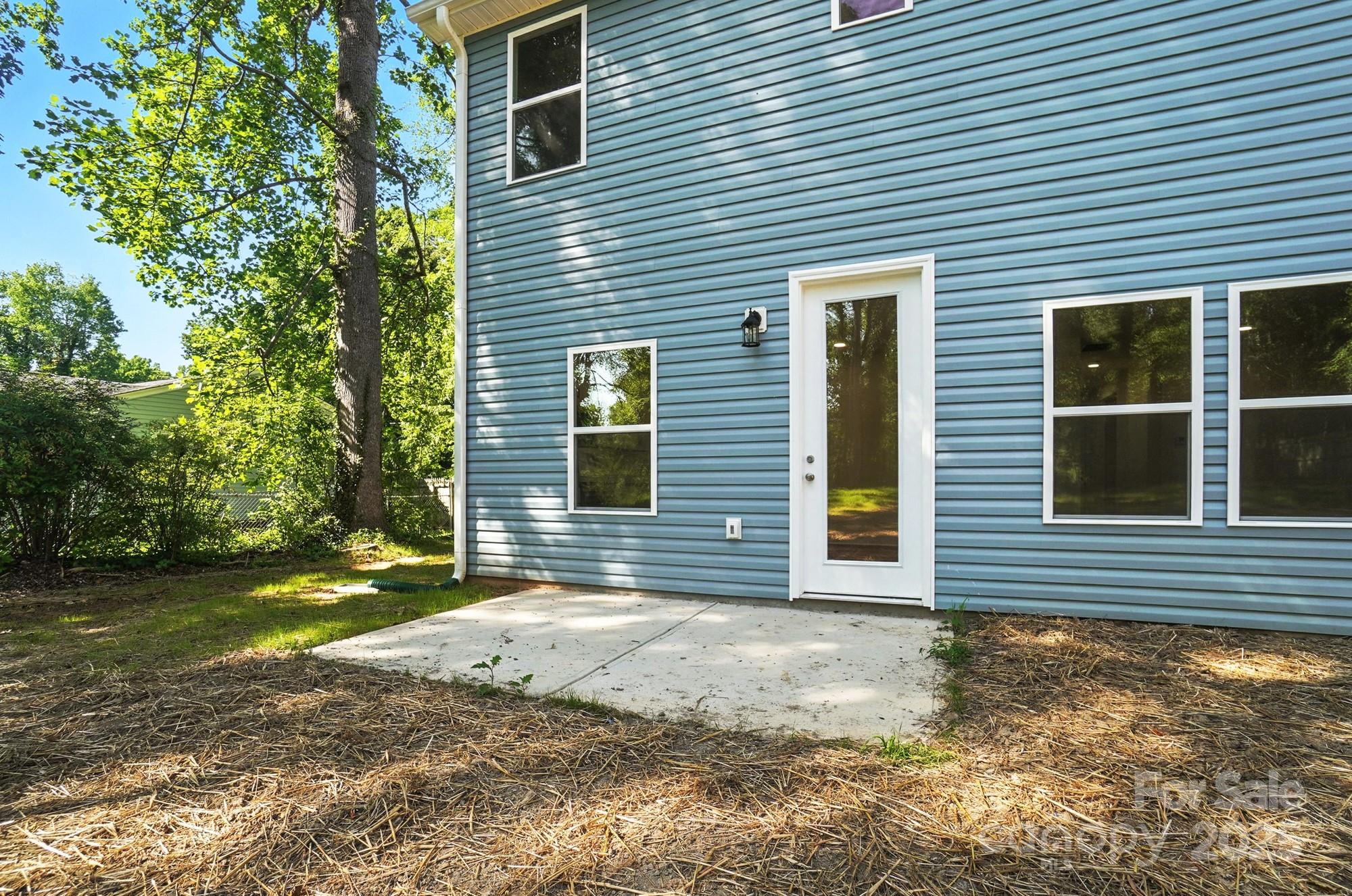 Blue-sided rear of a house with a glass-paneled door, white-trimmed windows, and a concrete patio.