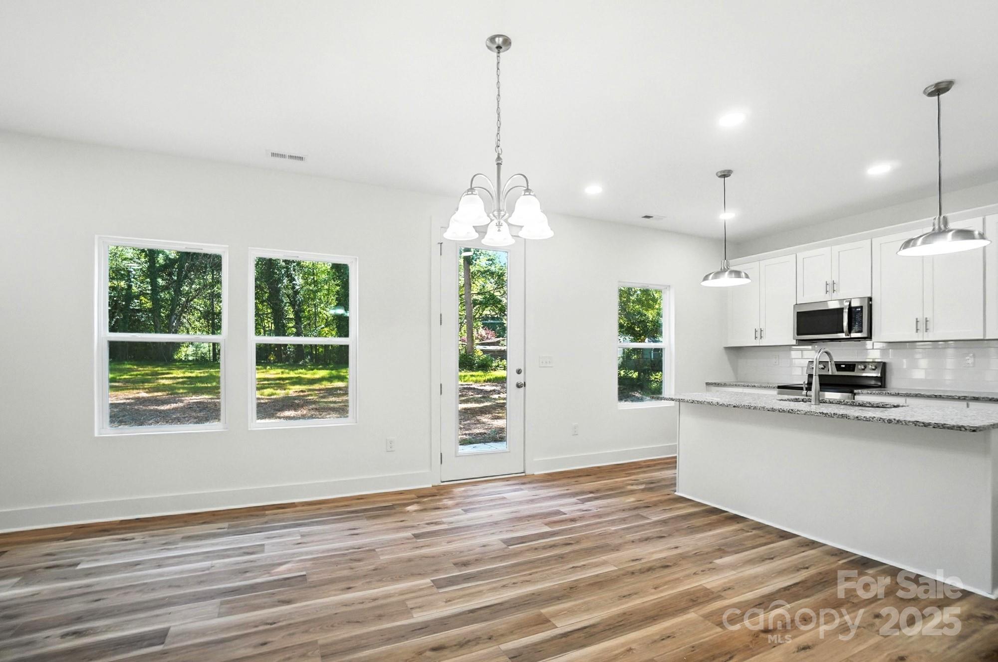 Unfurnished kitchen with white cabinets, granite peninsula, stainless steel appliances, and wood-look flooring.
