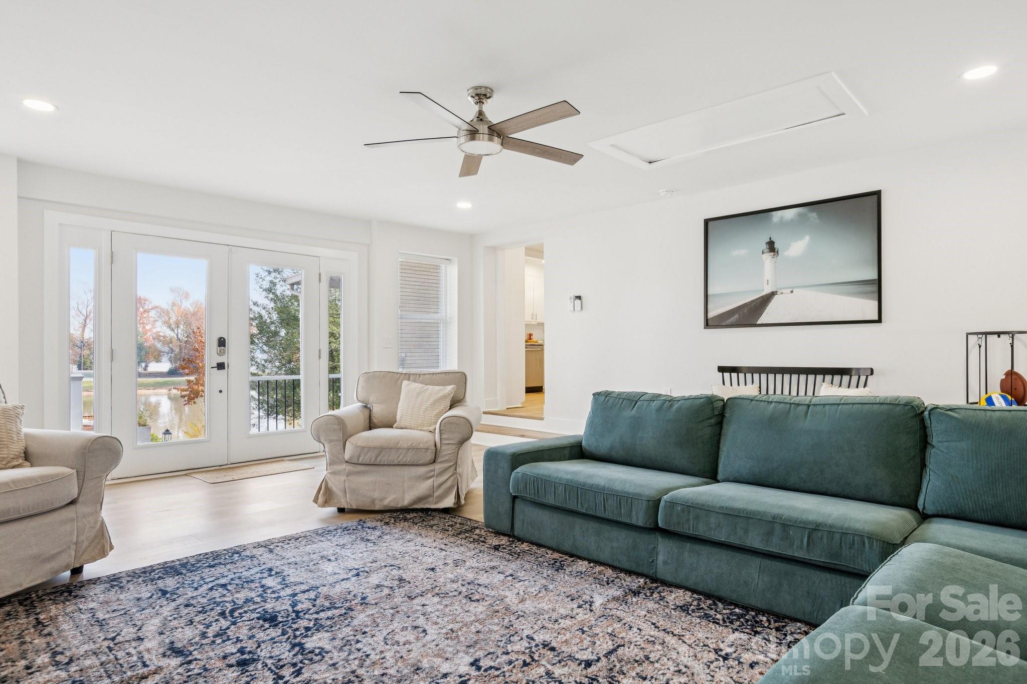 Living room with a teal sectional, beige armchairs, patterned rug, and glass doors overlooking water.